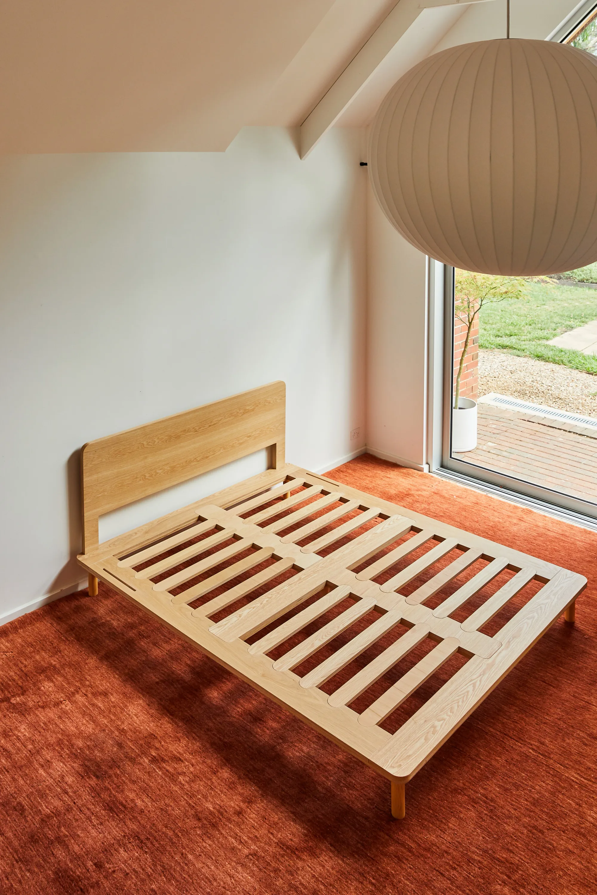 The Timber Bed Frame by Eva shown without a mattress on a red rug