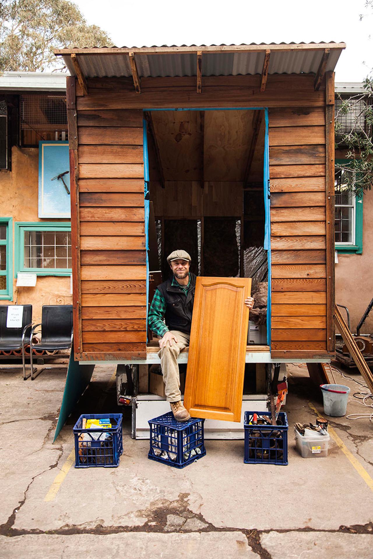 Tiny house on a trailer using recycled materials with builder showing materials