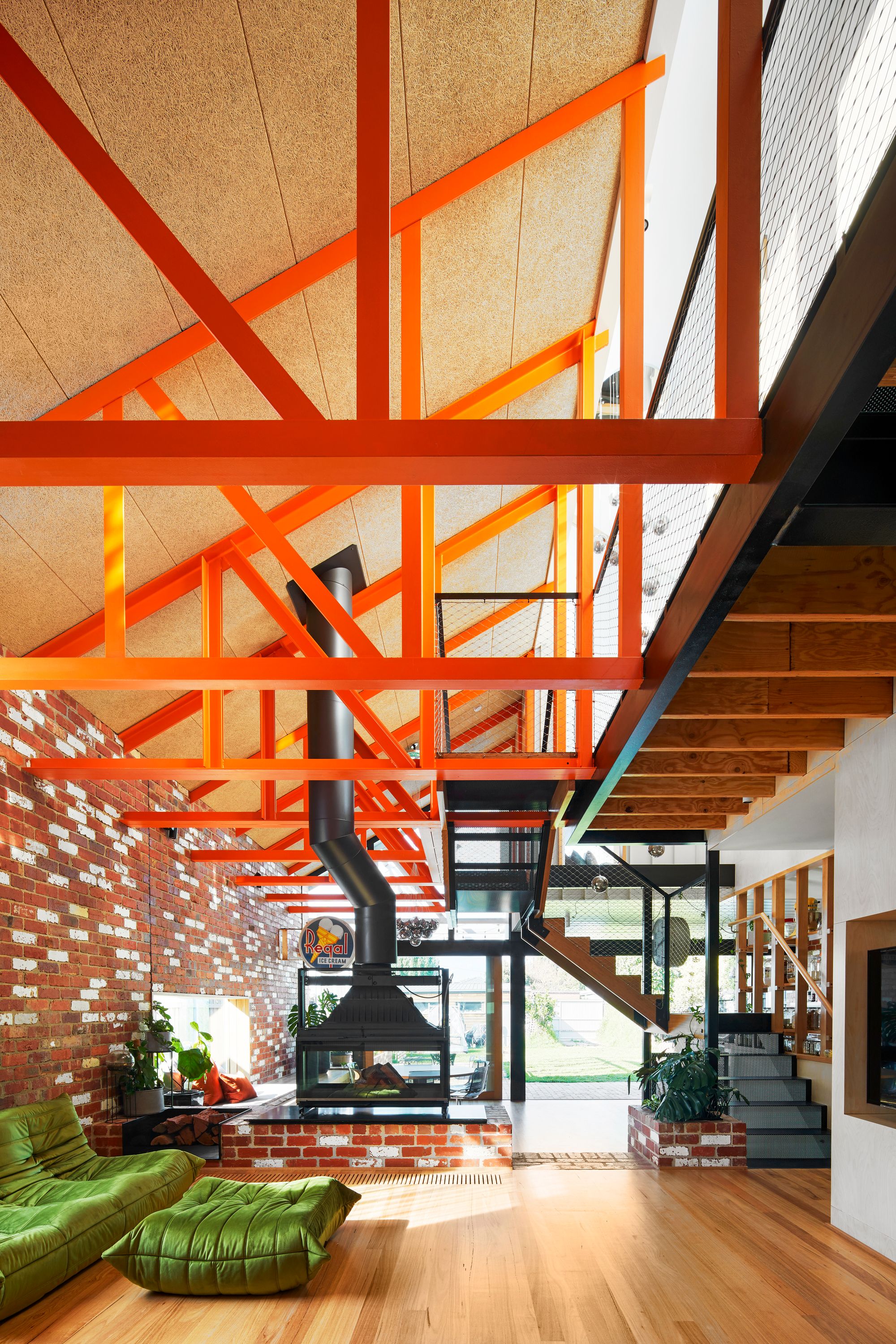 Gantry House by OOF! Architecture showing exposed roof trusses painted in orange over living room