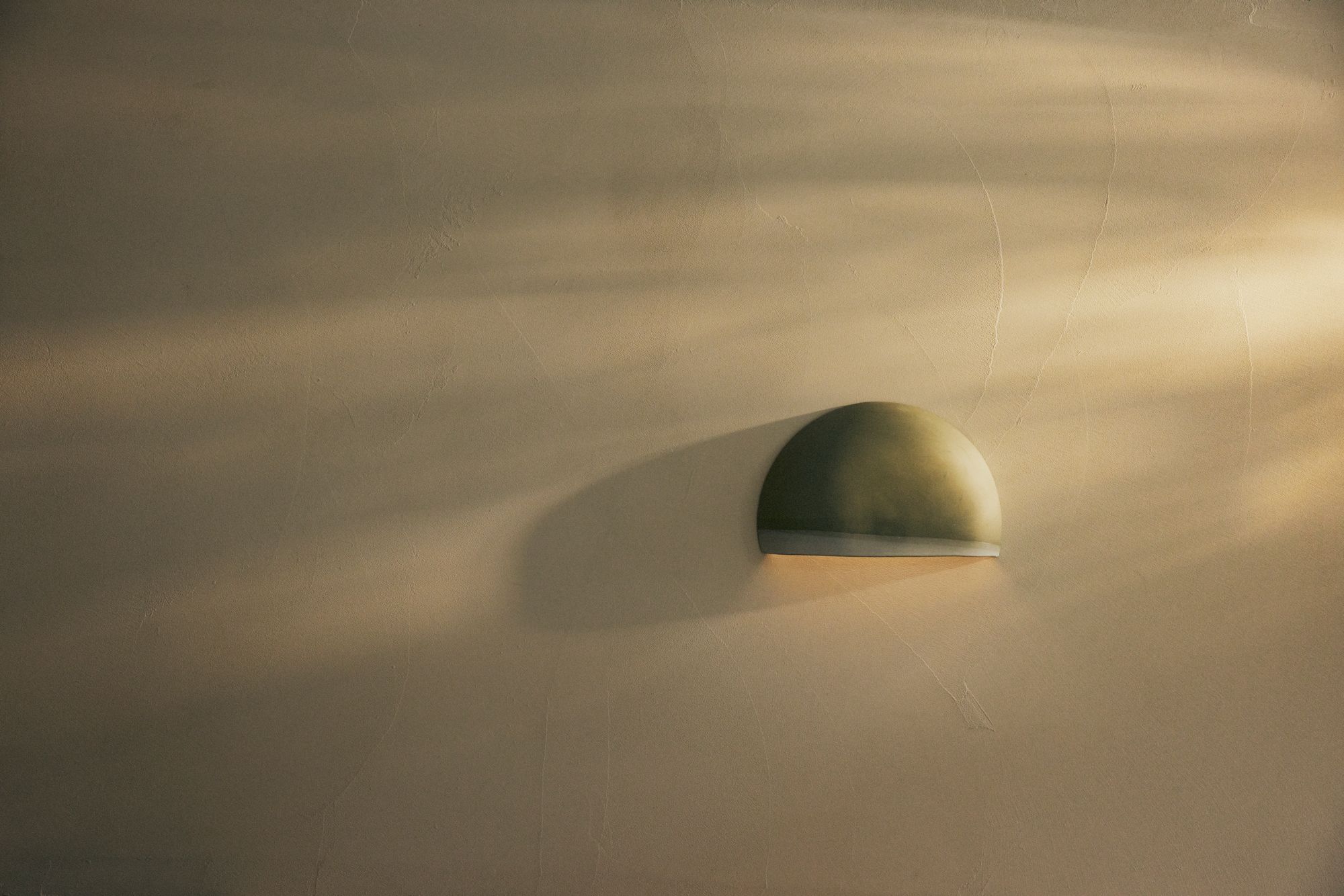 Studio Enti Cresent Sconce positioned as a single feature sconce, in a green tone. 