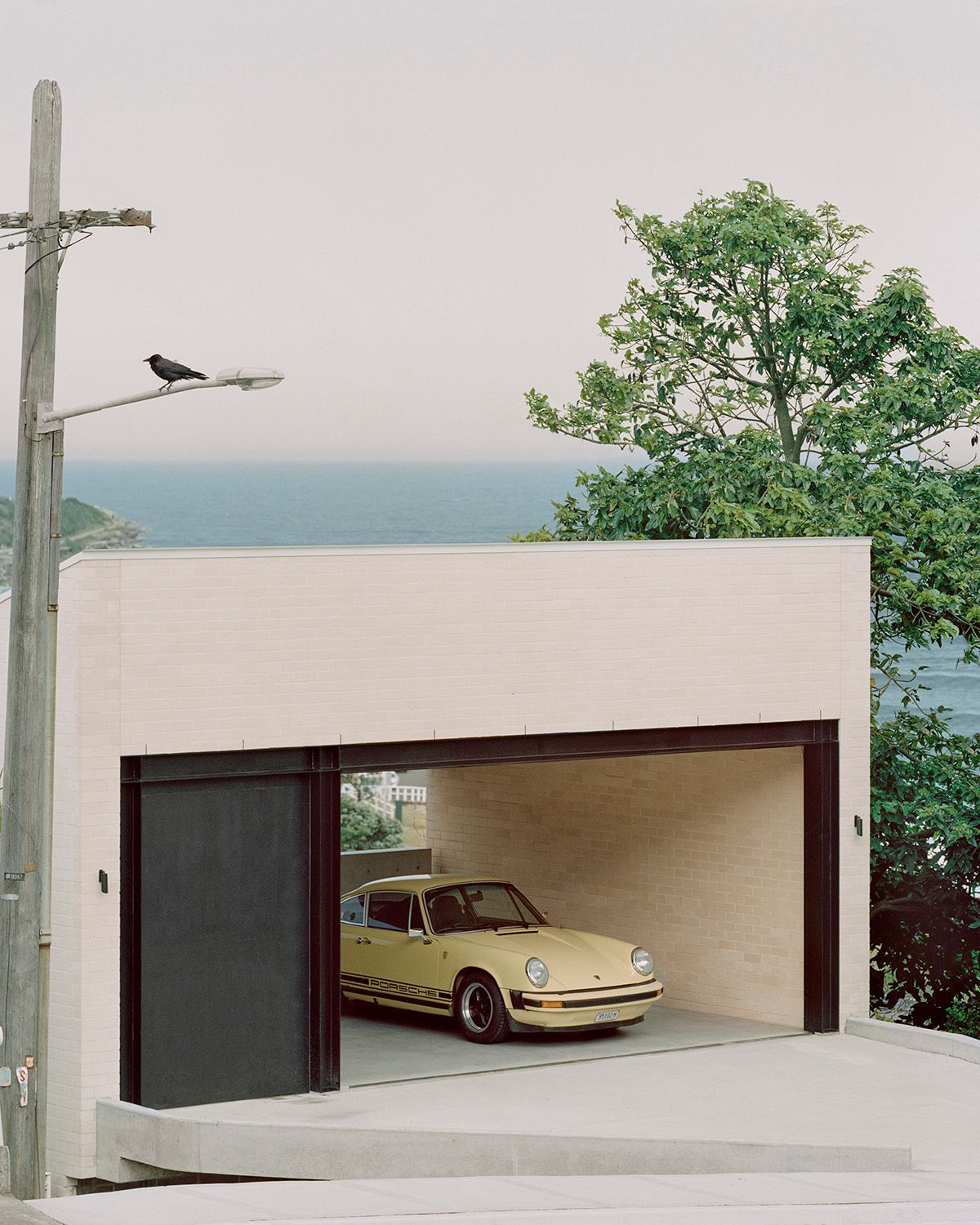 Bronte House by Tribe Studio Architects showing brick garage with a vintage yellow car parked in it