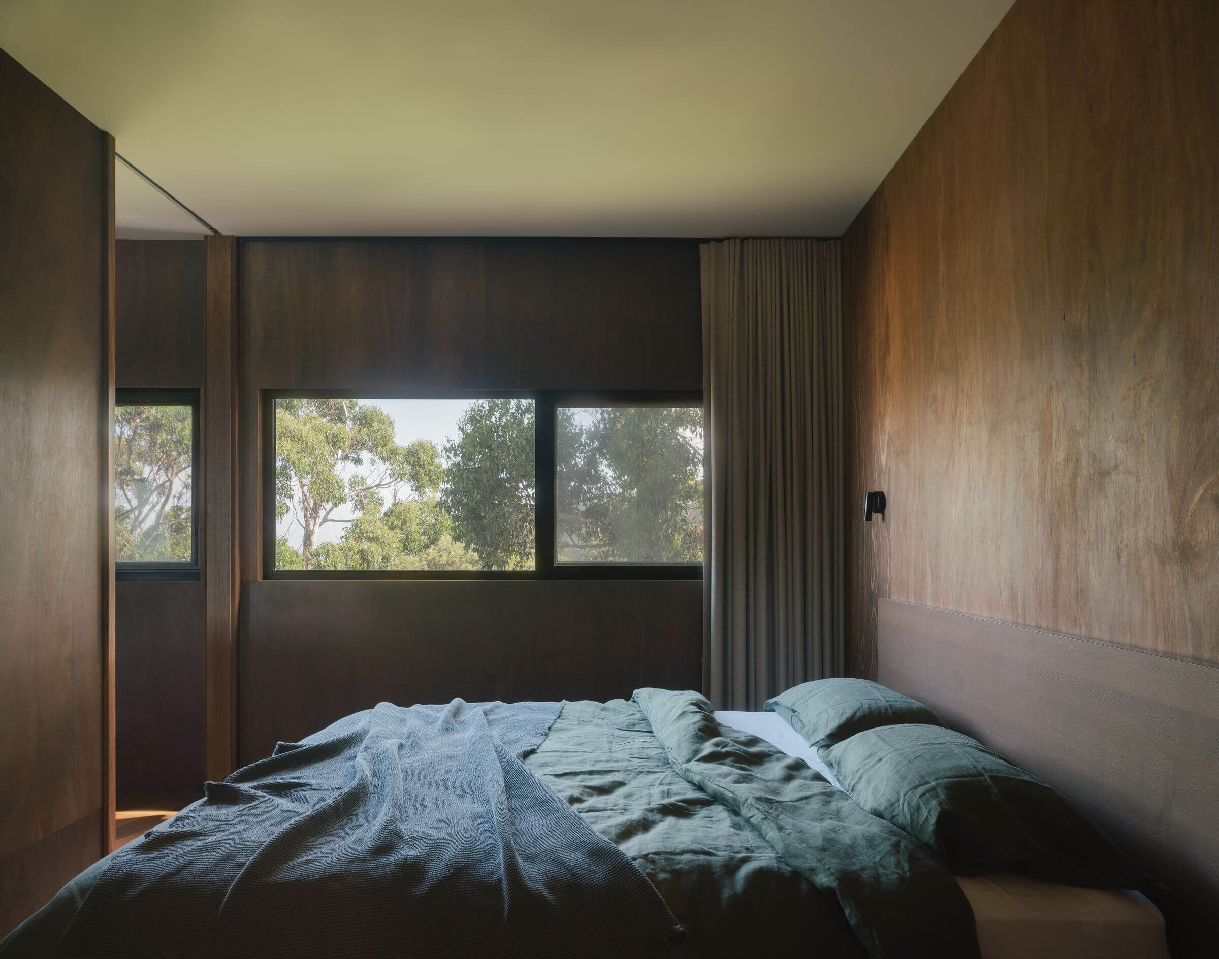 Kennett River House by MGAO showing timber lined bedroom looking out over trees