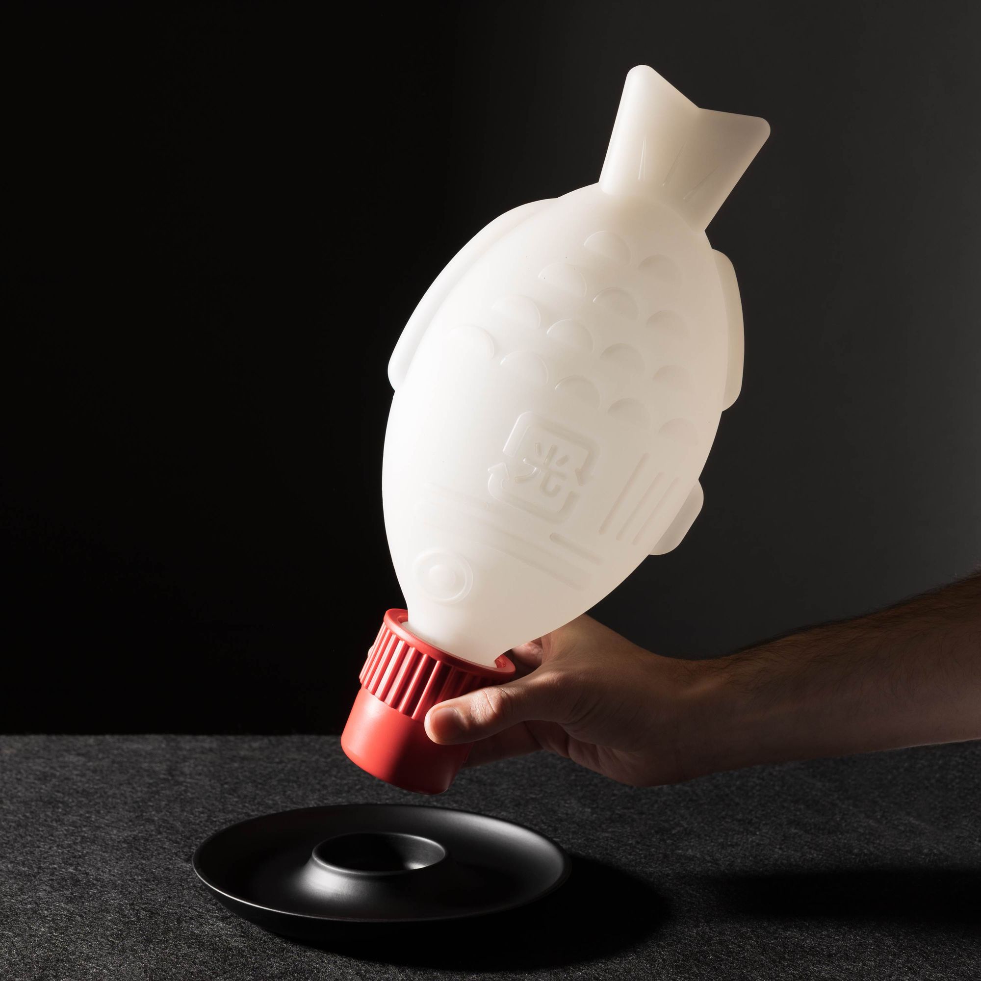 Light Soy by Heliograf showing a person removing the fish shaped lamp from its base plate