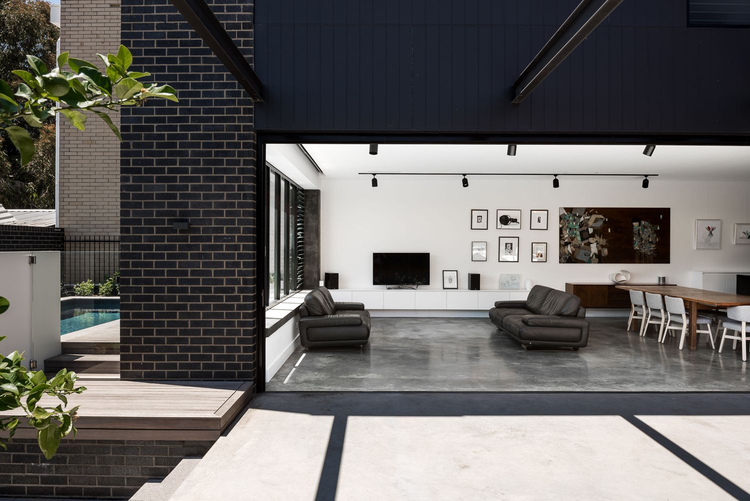 Urban House by Robeson Architects. Ultra modern indoor and outdoor living areas. Polished concrete interior with white walls and black furniture, feature lighting and window frames. Exterior area has concrete flooring, black brick walls and sunken pool in timber deck. 