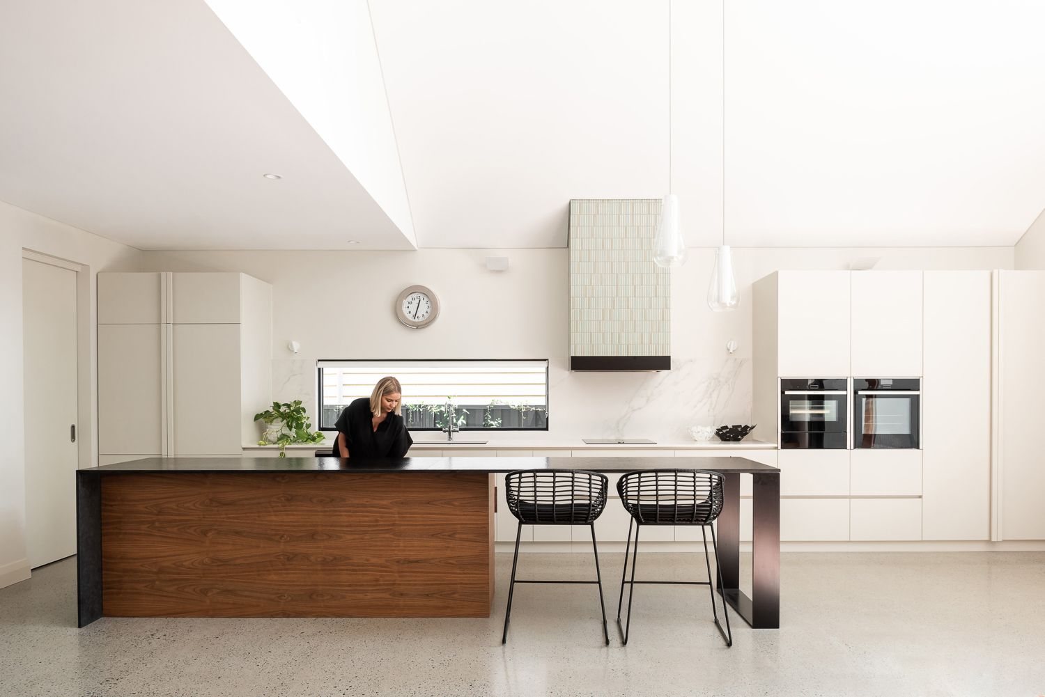 Subiaco House by Robeson Architects. Modern, minimalistic kitchen with white cabinetry and feature timber island bench with black metal benchtop. Whie warble floor-to-ceiling splashback. 