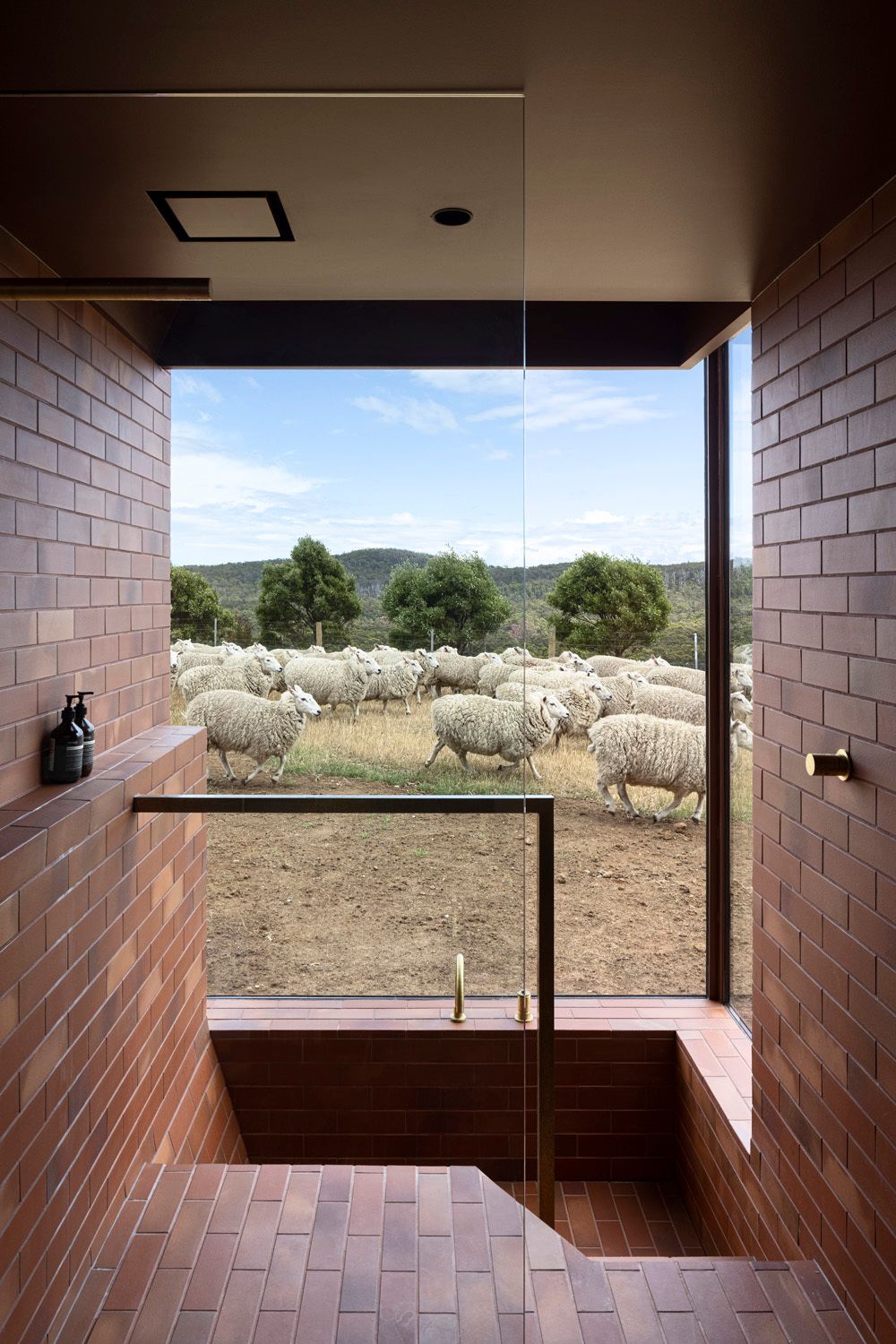 Coopworth by FMD Architects showing a red tiled bathroom with a sunken bath tub that overlooks a rural farm