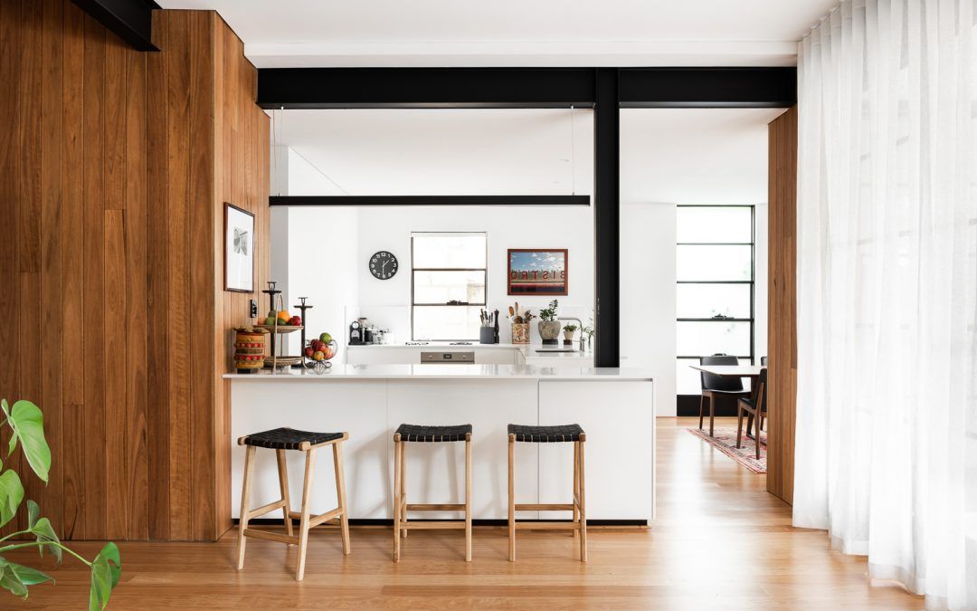 Cottesloe Apartment Renovation MDC Architects. Detailed shot of mid century modern kitchen. Timber floors and wall pannelling. Black exposed industrial beams. White curtains. Leather and timber bar stools. White kitchen bench and cabinetry. 