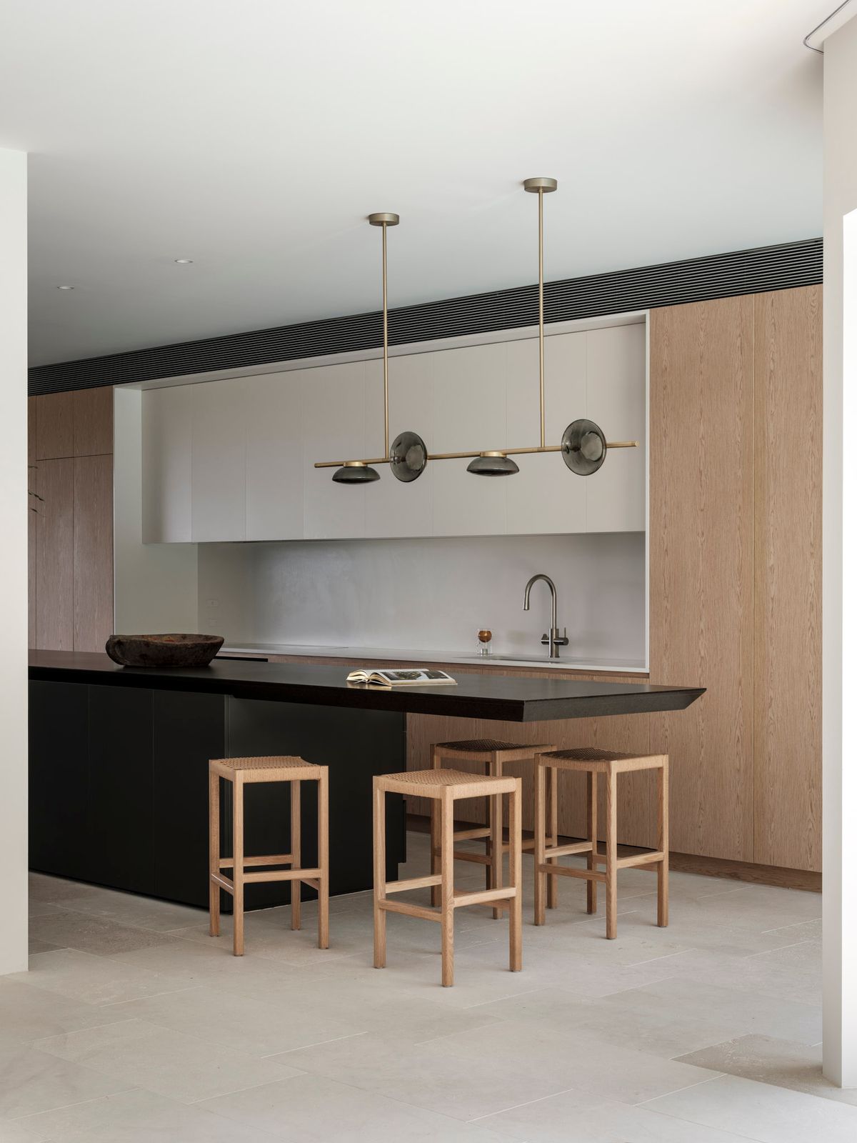 A sleek modern kitchen island design that has a tapered black stone benchtop that is cantilevered to provide a dining space