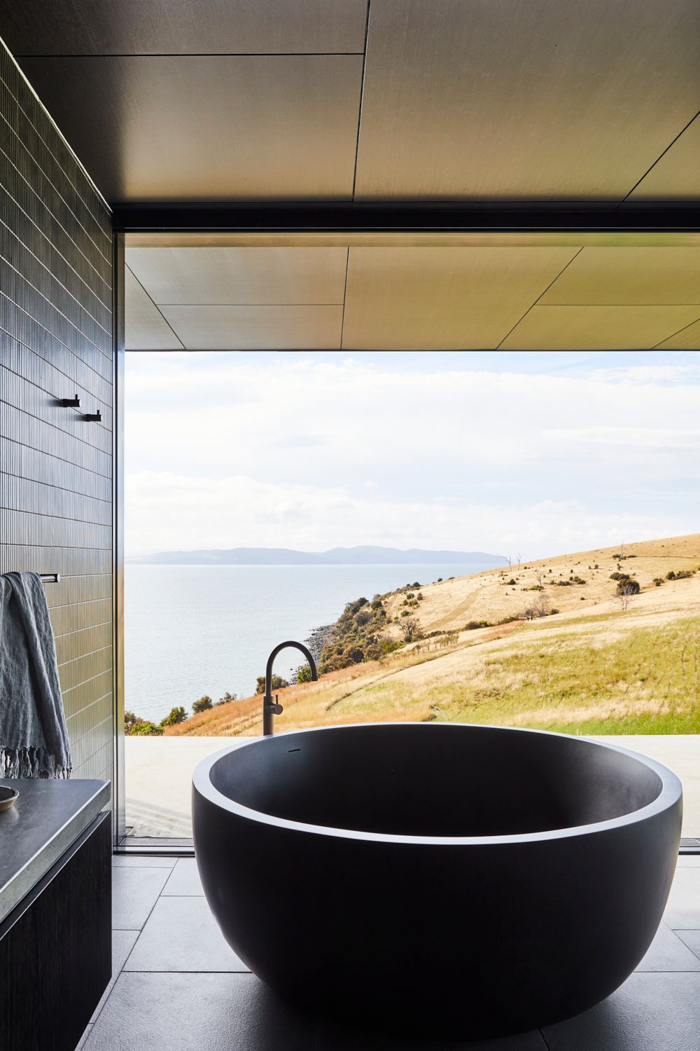 The Point Tasmania by Tanner Architects showing a round bathtub that overlooks an ocean view and rolling hills