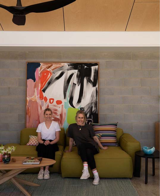 Architects Lauren Benson (Left) and Simone Robeson (Right) sitting on a sofa and smiling in front of artwork