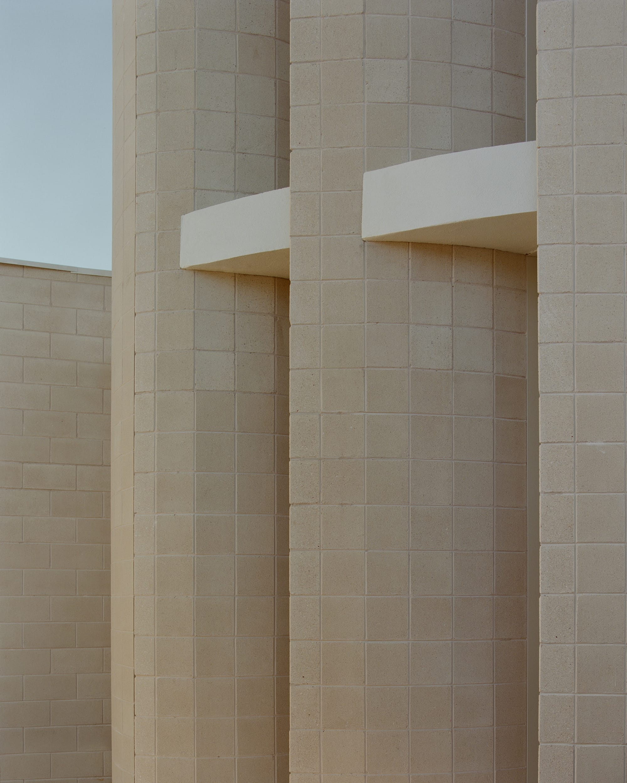 The photo captures a detail of the building's exterior, showing the texture of the beige bricks and two rectangular white ledges against a clear sky.