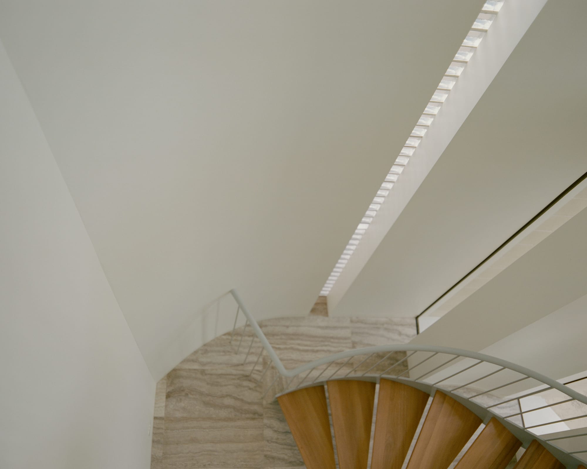 An interior shot showcases a staircase with light wood steps, white walls, and a curved ceiling with a skylight that allows natural light to stream in.
