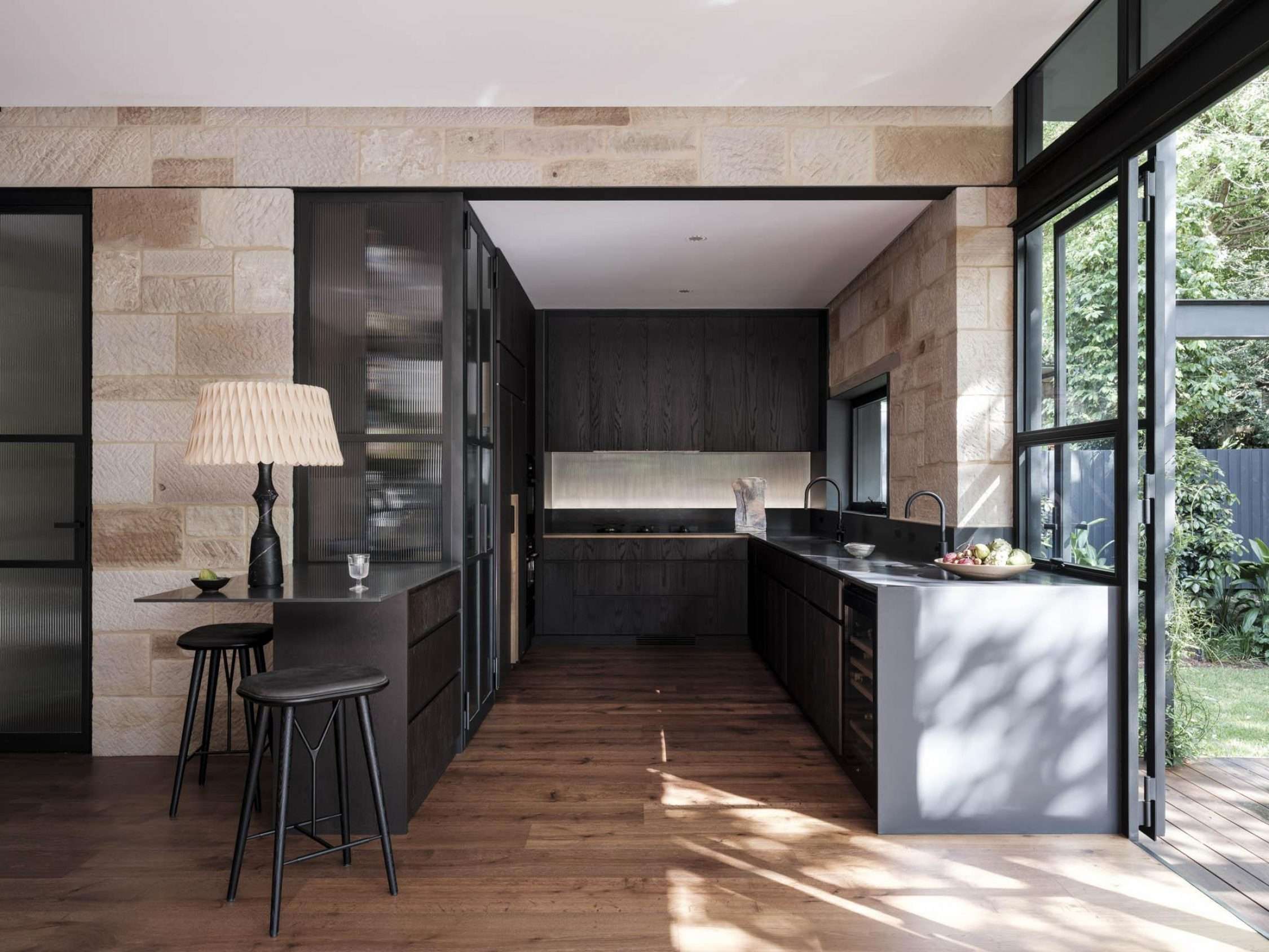 Maranatha House by BIJL Architecture showing an interior view of the kitchen with sandstone walls and dark timber joinery