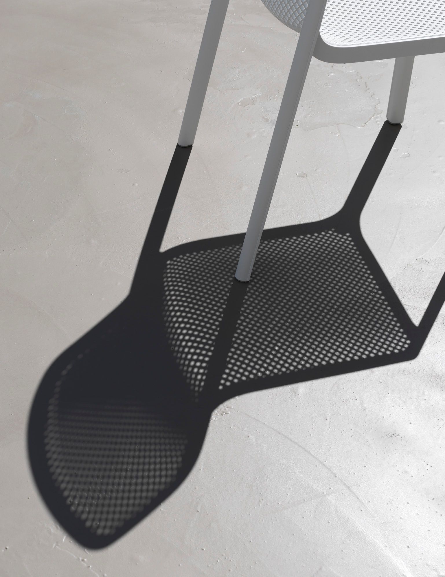 Remarkable Outdoor Living: Nadi Bit Outdoor Resin Dining Chair inn Anthracite.A shadow of a perforated metal chair cast on a textured concrete floor, with sunlight creating a patterned effect that mimics the chair's design.