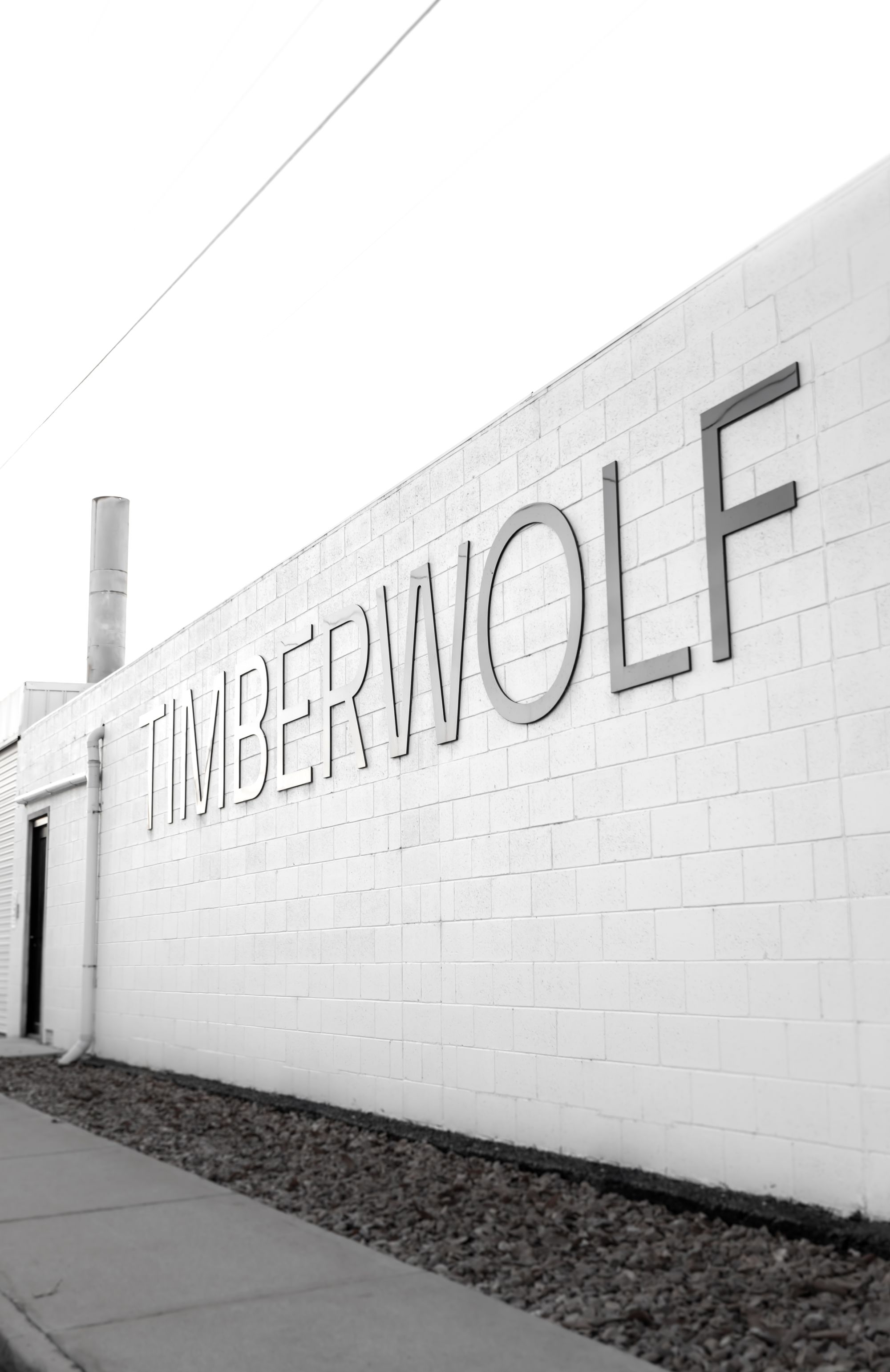 Timberwolf Design Showroom. the exterior of the Timberwolf showroom, with the brand name "TIMBERWOLF" prominently displayed in bold, three-dimensional letters on a white brick wall. The composition of the image, with a clear sky as the backdrop and a focus on the brand signage, suggests a modern and professional business facade. This branding is likely meant to convey a strong and reliable image for the company.