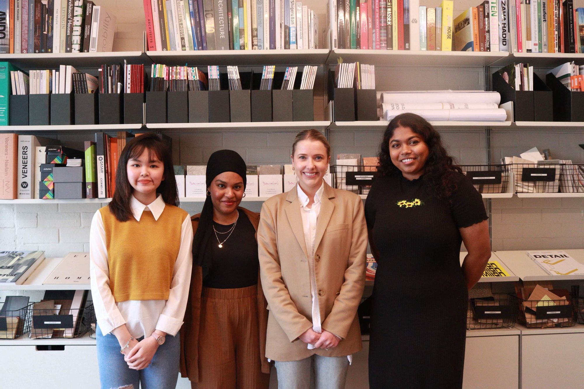 Architect Lauren Benson with Curtin University students. Four women smiling and standing on front of a bookshelf. 