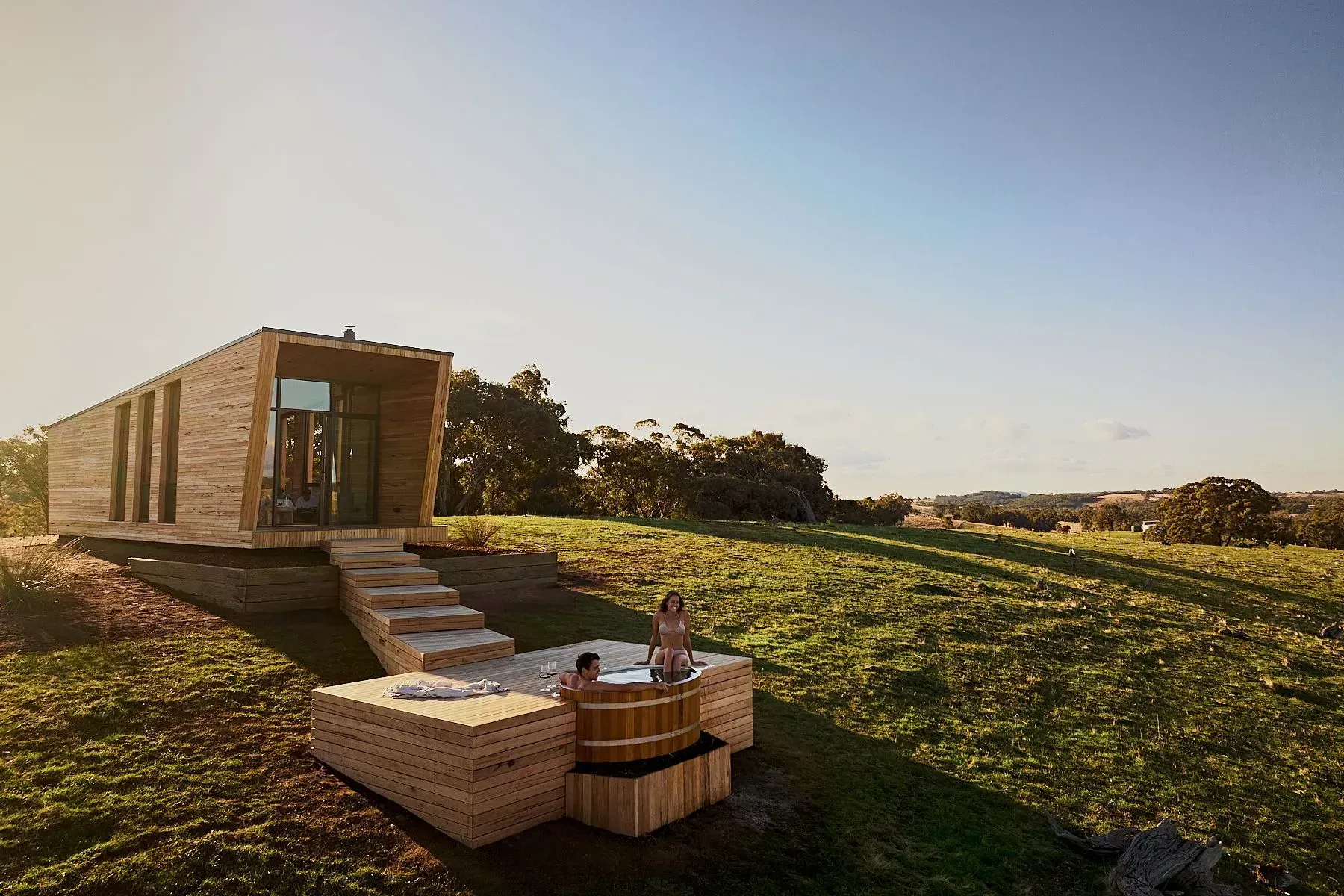 Heathcote by Wilka Eco Escapes showing the timber cabin sitting in the landscape with two people in the timber spa bath