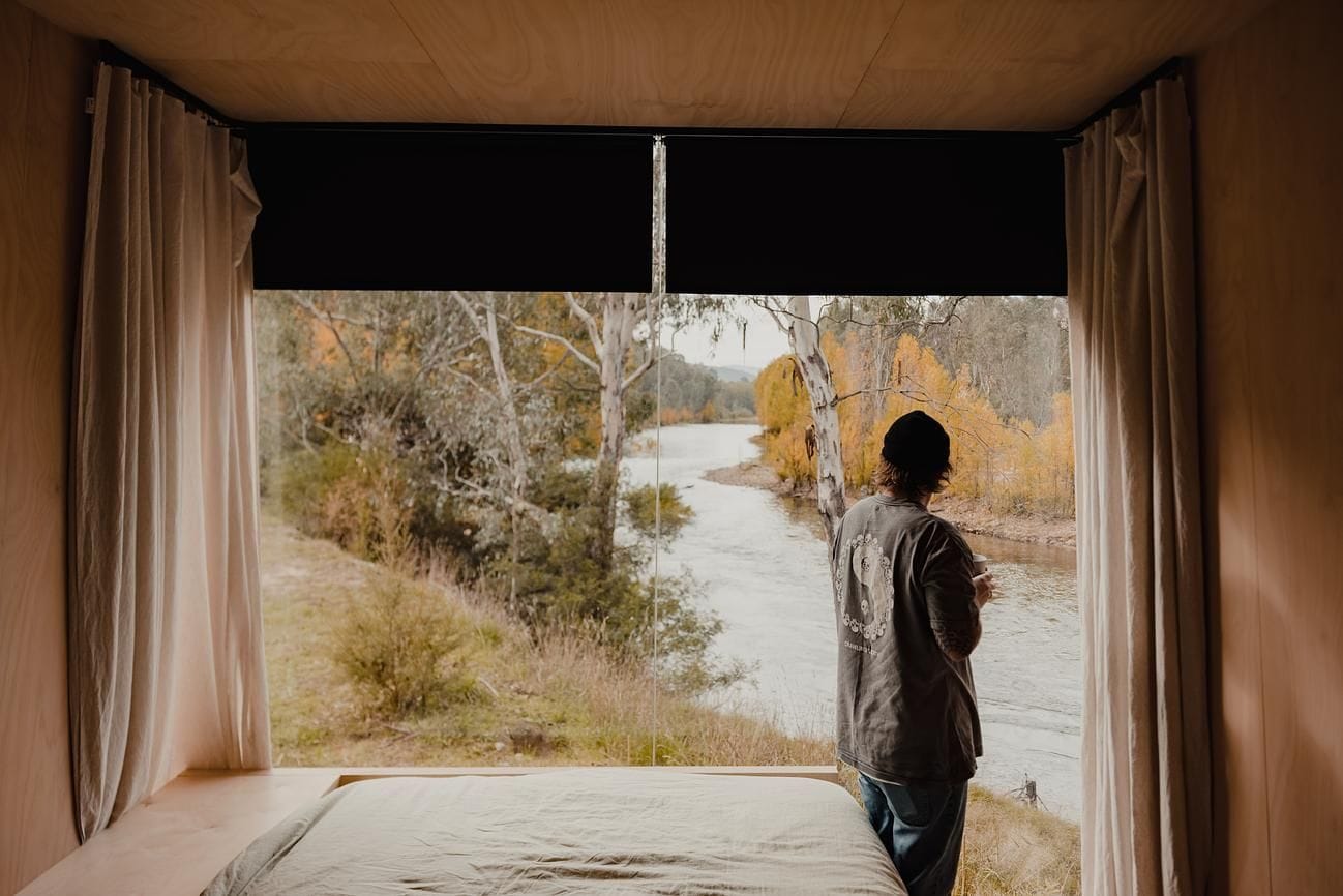 Cortes Cabin in Gapsted showing the interior view of the bedroom with a person looking out to the river and landscape in the background