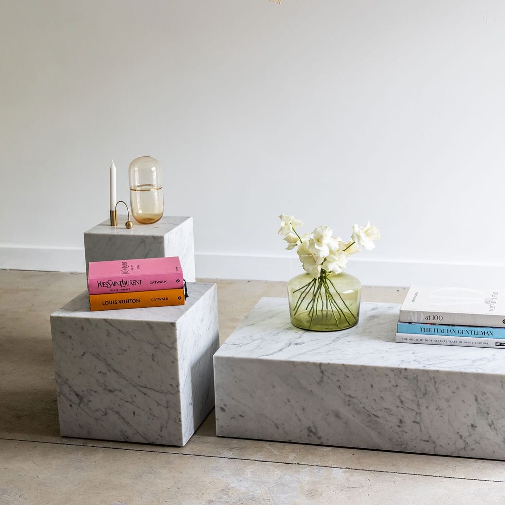 Noma Co Studio. Copyright of Noma Co Studio. White marble cube and white marble rectangle furniture pieces. Styled with range of vivid coloured books and vases with white flowers. Concrete floor and white walls in space. 