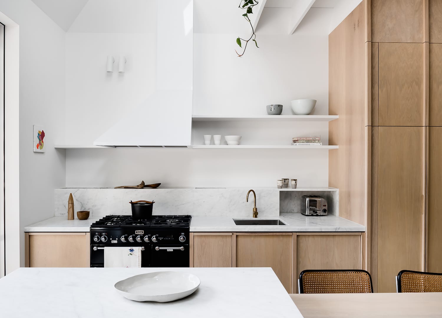 Storybook House by Folk Architects. Phtography by Tom Blachford. Landscape image of residential kitchen. Light timber cabinetry. White walls. Subtle marble countertop and splashback. Black oven and brass tapware. 