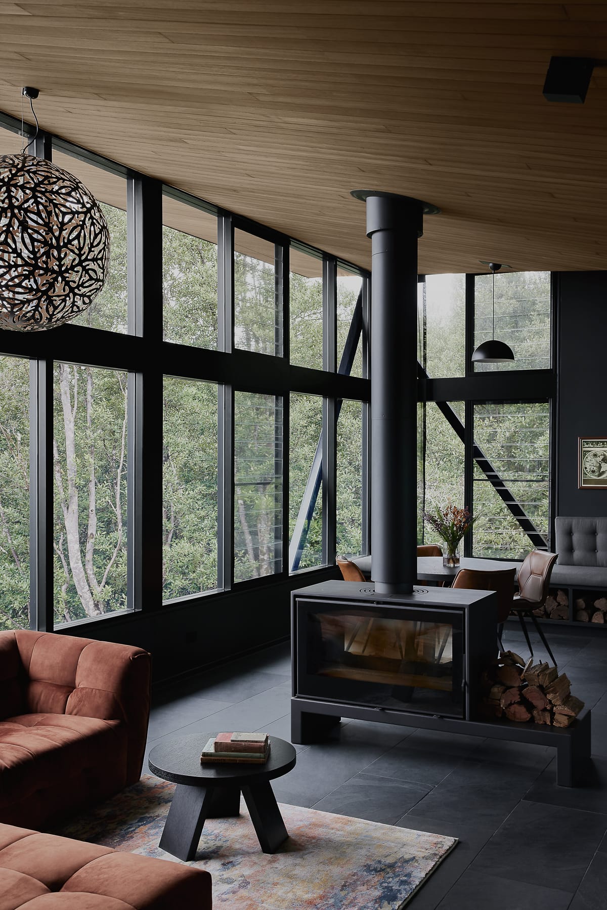 Cloudview Springbrook by Paul Uhlmann Architects. Photography by Brock Beazley. Contemporary living space with black floor tiles and black framed windows that overlook a rainforest. Black fireplace in centre of room. 