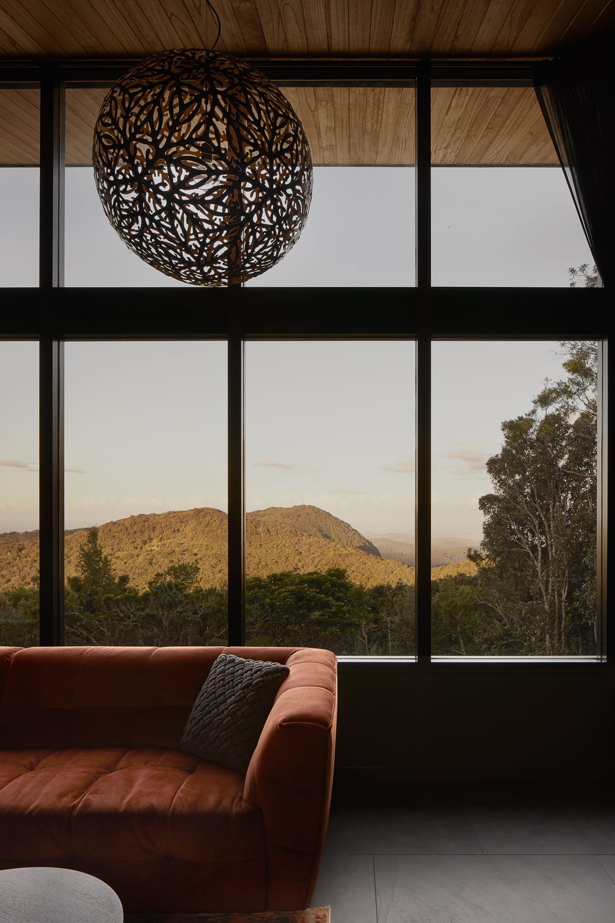 An interior shot of the living room showing an orange sofa in the foreground and the view of the mountain rainforest in the background