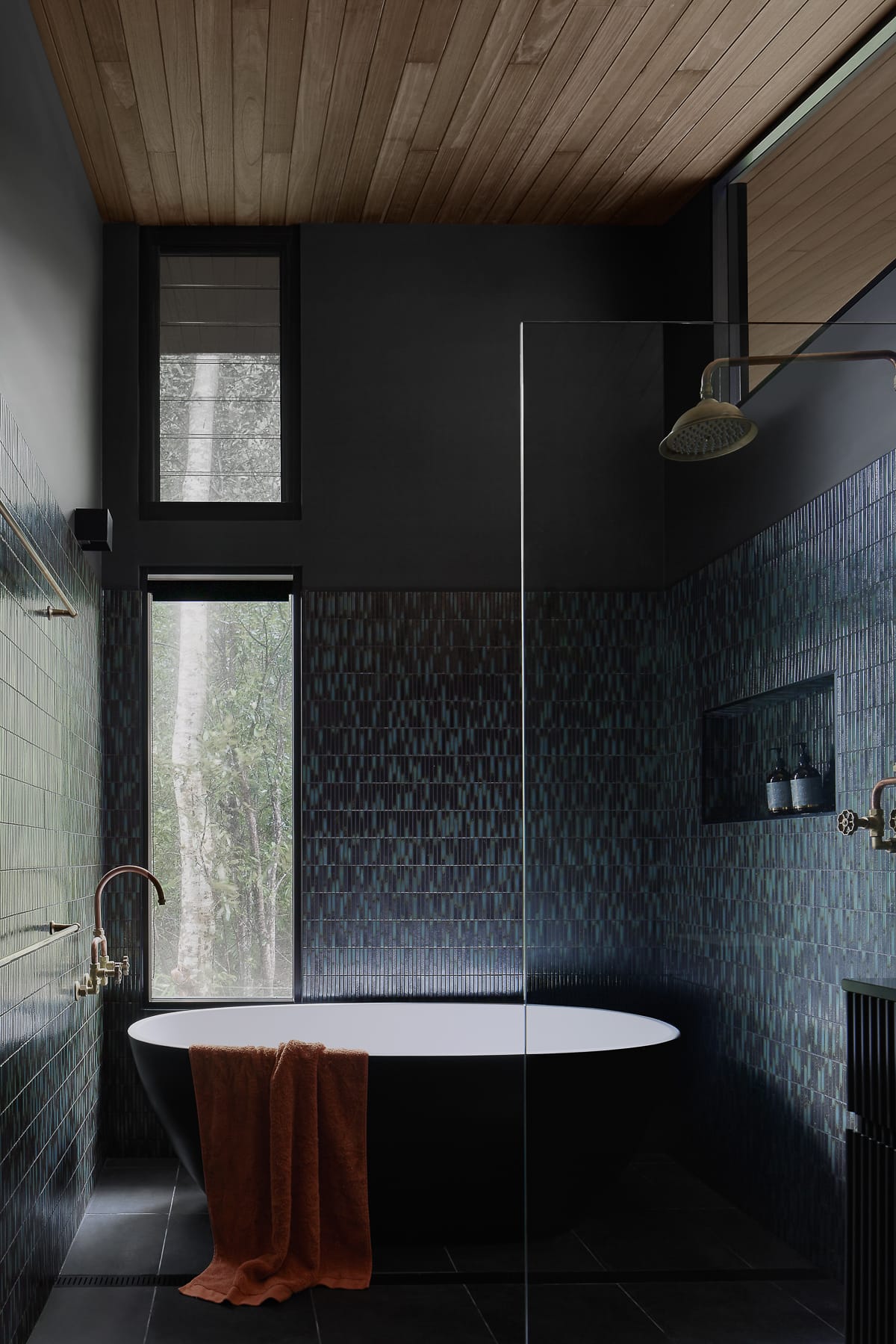 Cloudview Springbrook by Paul Uhlmann Architects. Photography by Brock Beazley. Bathroom with dark mosaic wall tiles and black floor tiles. Black, freestanding bathtub in centre of room.