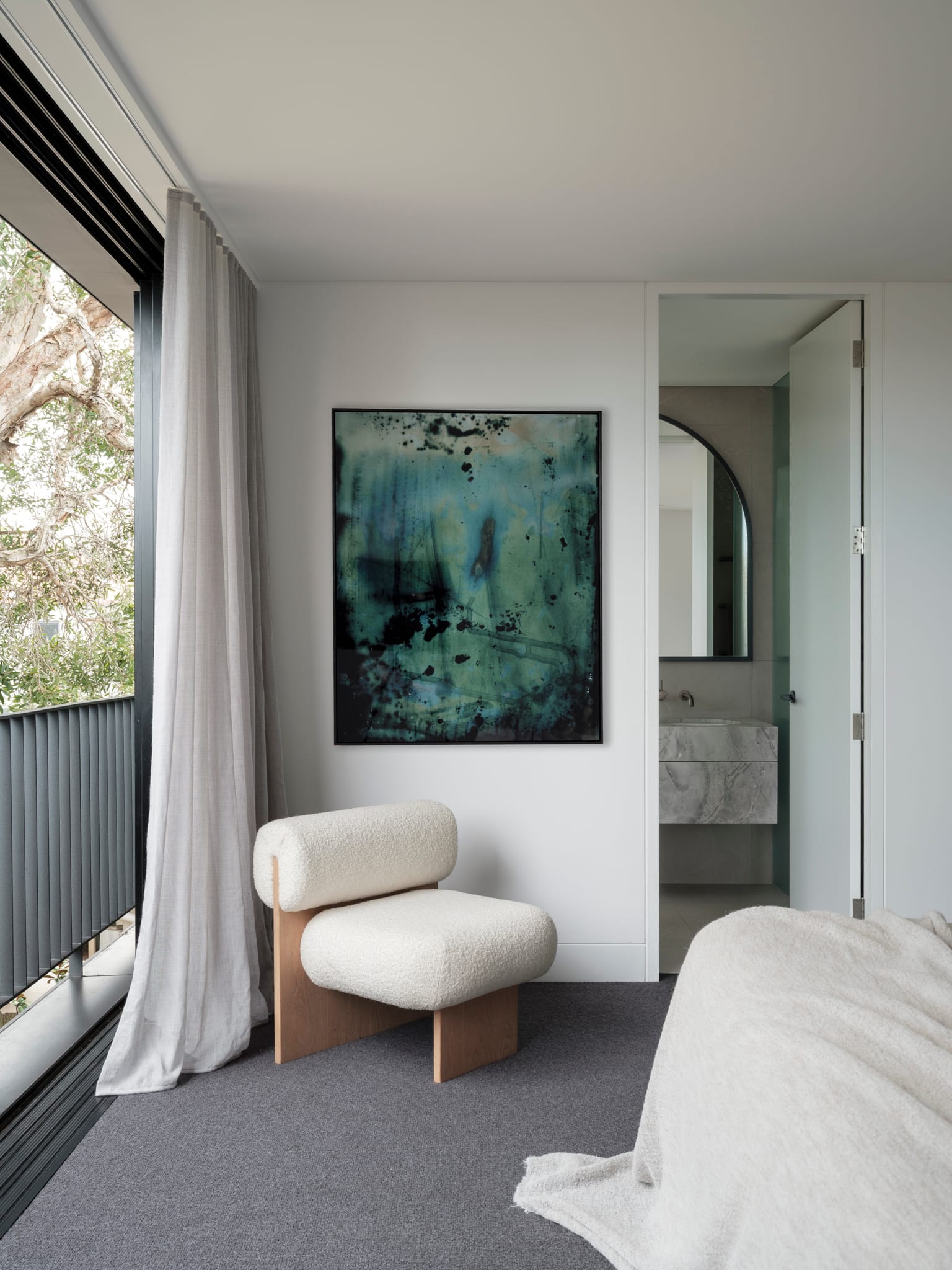 Bellevue House by Carla Middleton Architects. Photography by Tom Ferguson. Bedroom with grey carpet and white walls. White armchair. Balcony to the left and bathroom to the right. 