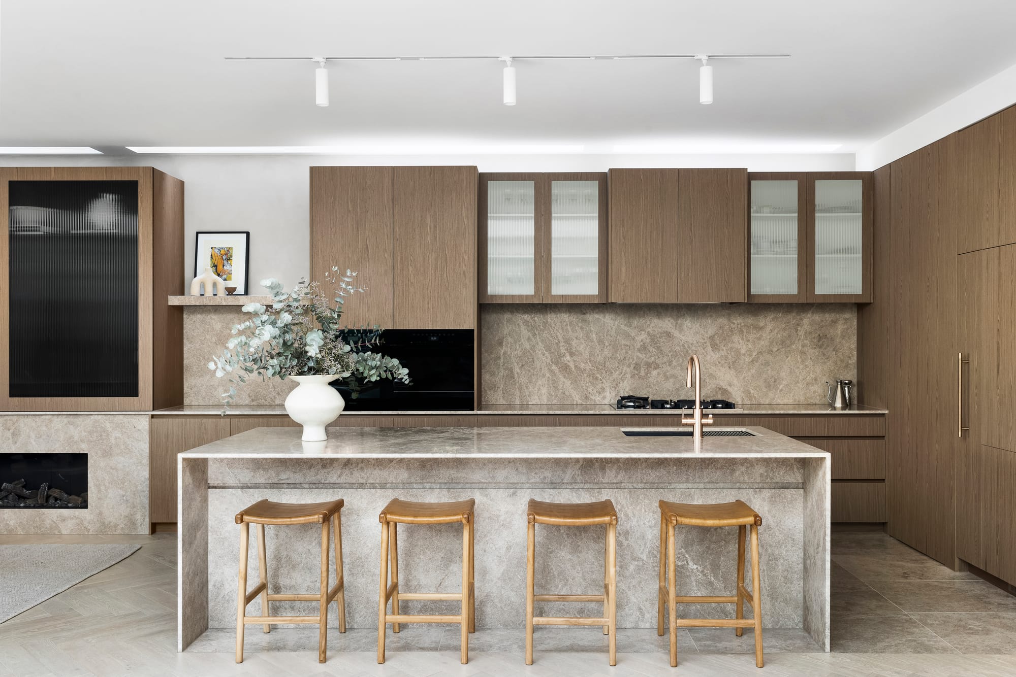 Goldsmith Residence by C.Kairouz Architects. Photography by Spacecraft. Kitchen with timber cabinetry. Stone island bench and splashback. Timber stools at island. Stone floors. 