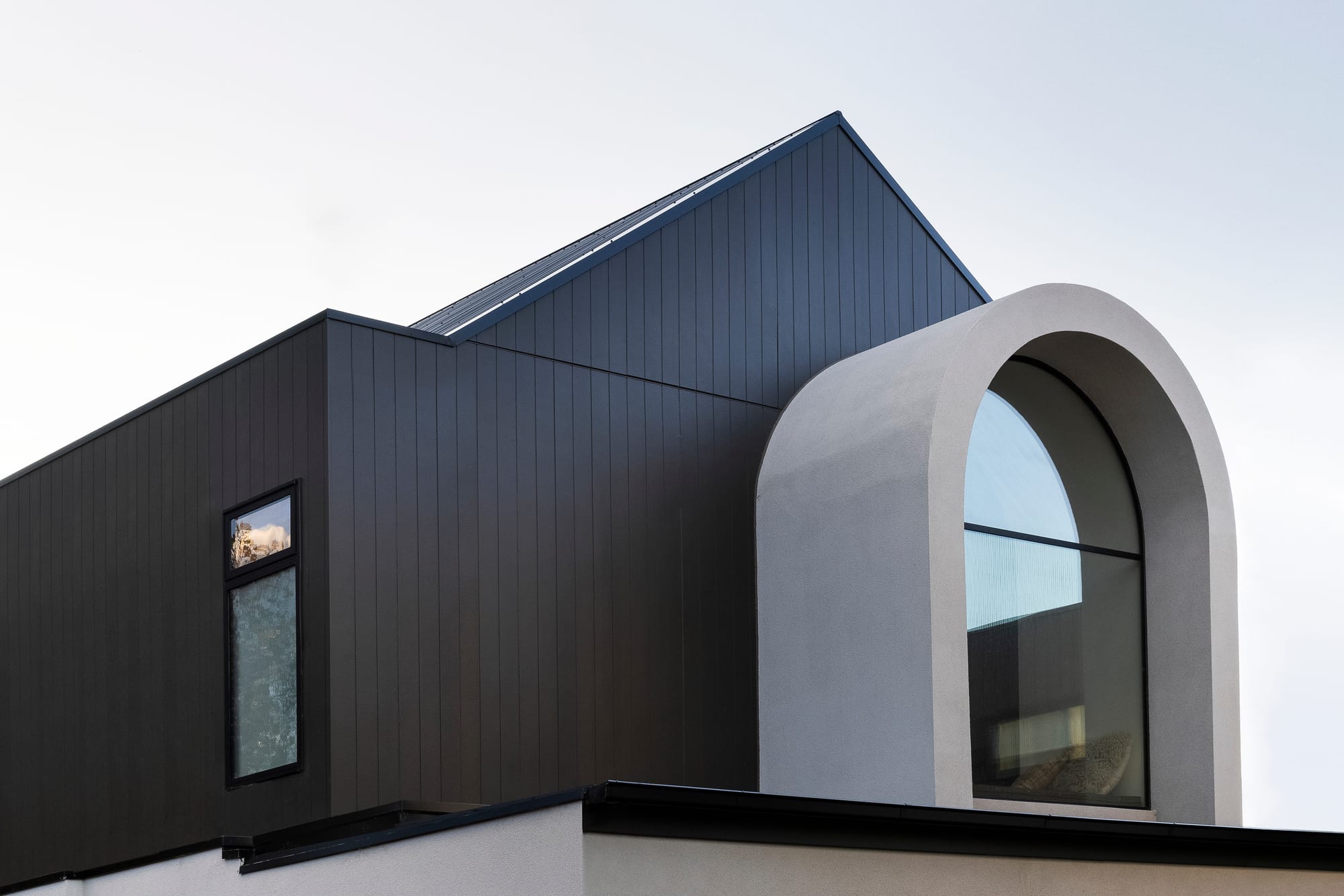Goldsmith Residence by C.Kairouz Architects. Photography by Spacecraft. Second storey facade with gabled roof and large, concrete arched window. Second storey finished in black timber clad. 