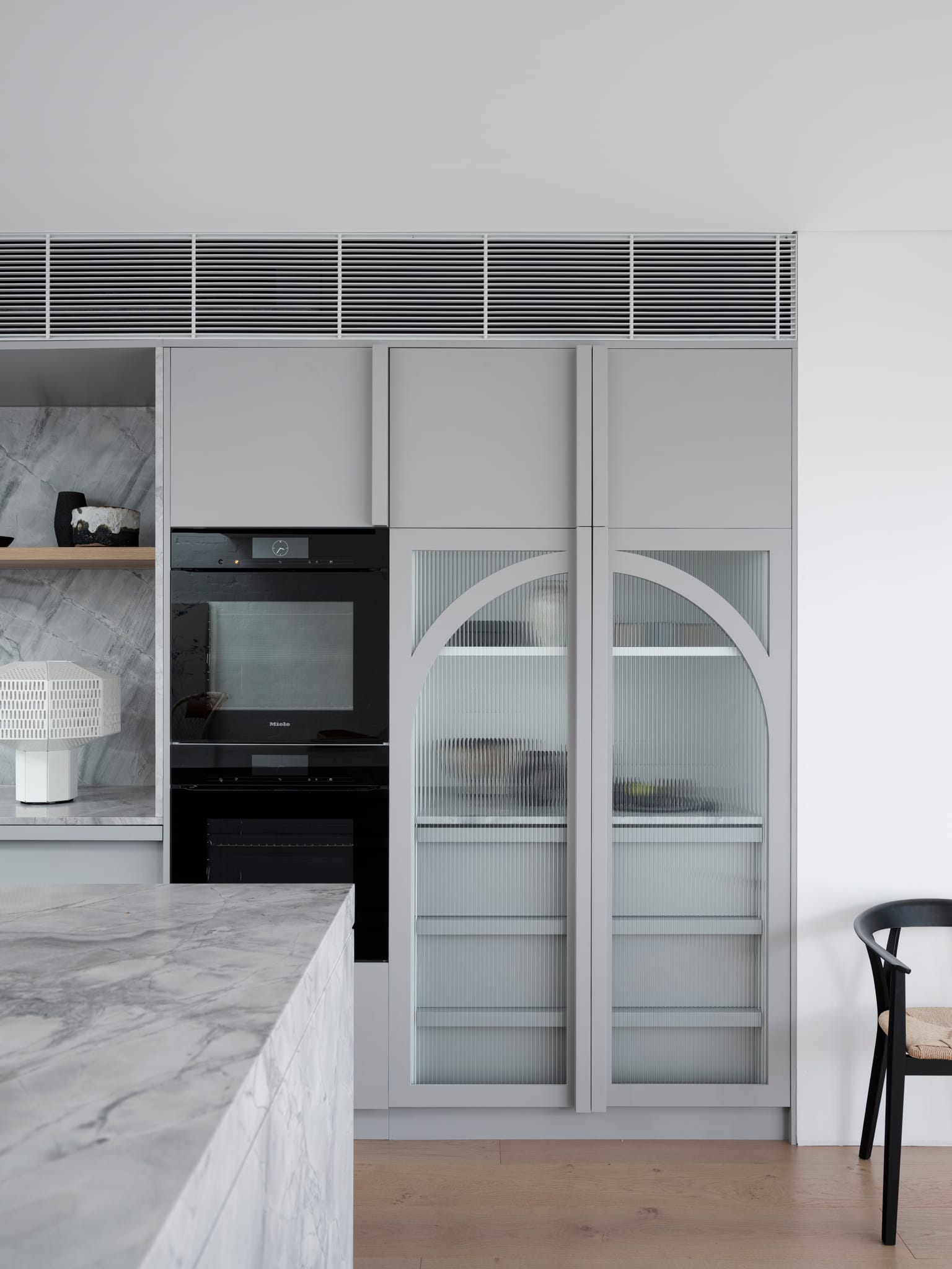 Bellevue House by Carla Middleton Architects. Photography by Tom Ferguson. Grey arched doorway cabinetry with fluted glass in kitchen. Marble island bench. Timber floors. 