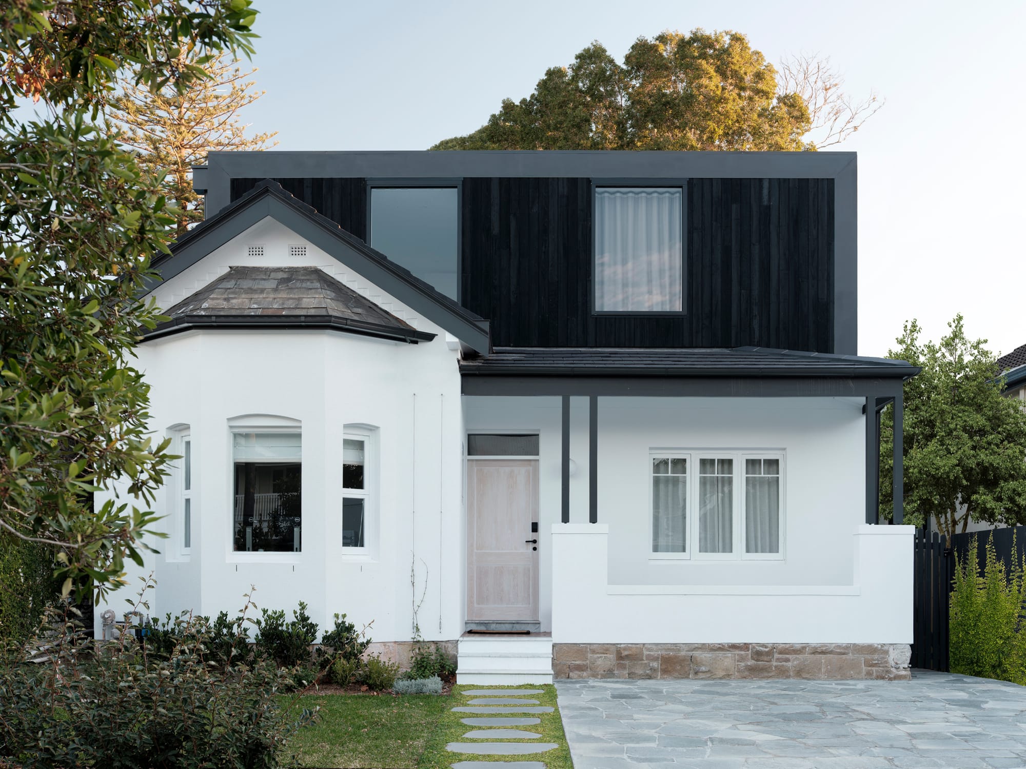 Bellevue House by Carla Middleton Architects. Photography by Tom Ferguson. Front facade of double storey residential home. Federation-style white ground floor. Contemporary black clad second storey. 