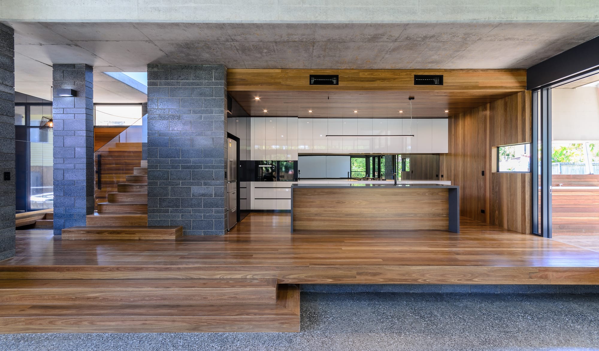 B Residence by 77 Architecture. Copyright of 77 Architecture. Ladnscape image of residential kitchen with elevated timber flooring, walls, ceiling and cabinetry. Dark brick.