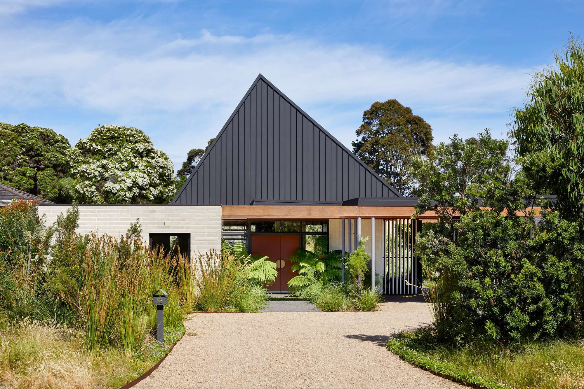 An exterior shot of the front of the house showing the high pitched roof in metal and brickwork walls withe garden surrounding