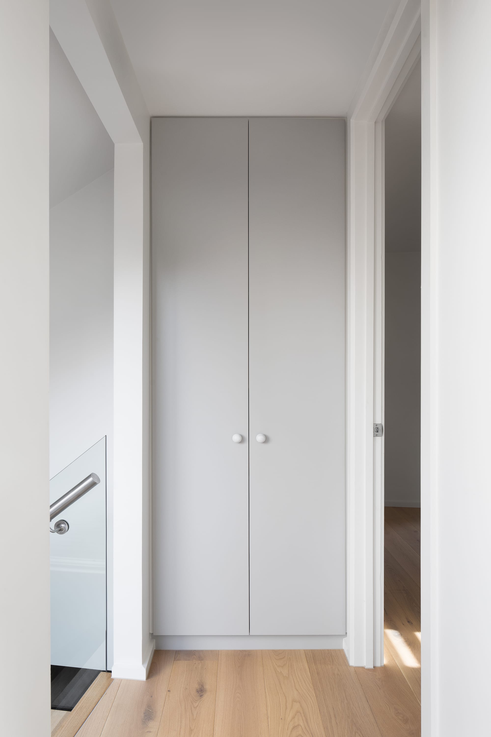 Stead House by Hannaford Design Studio. Photography by Emily Bartlett. Grey integrated cupboard with double doors. Timber floors. White walls. 