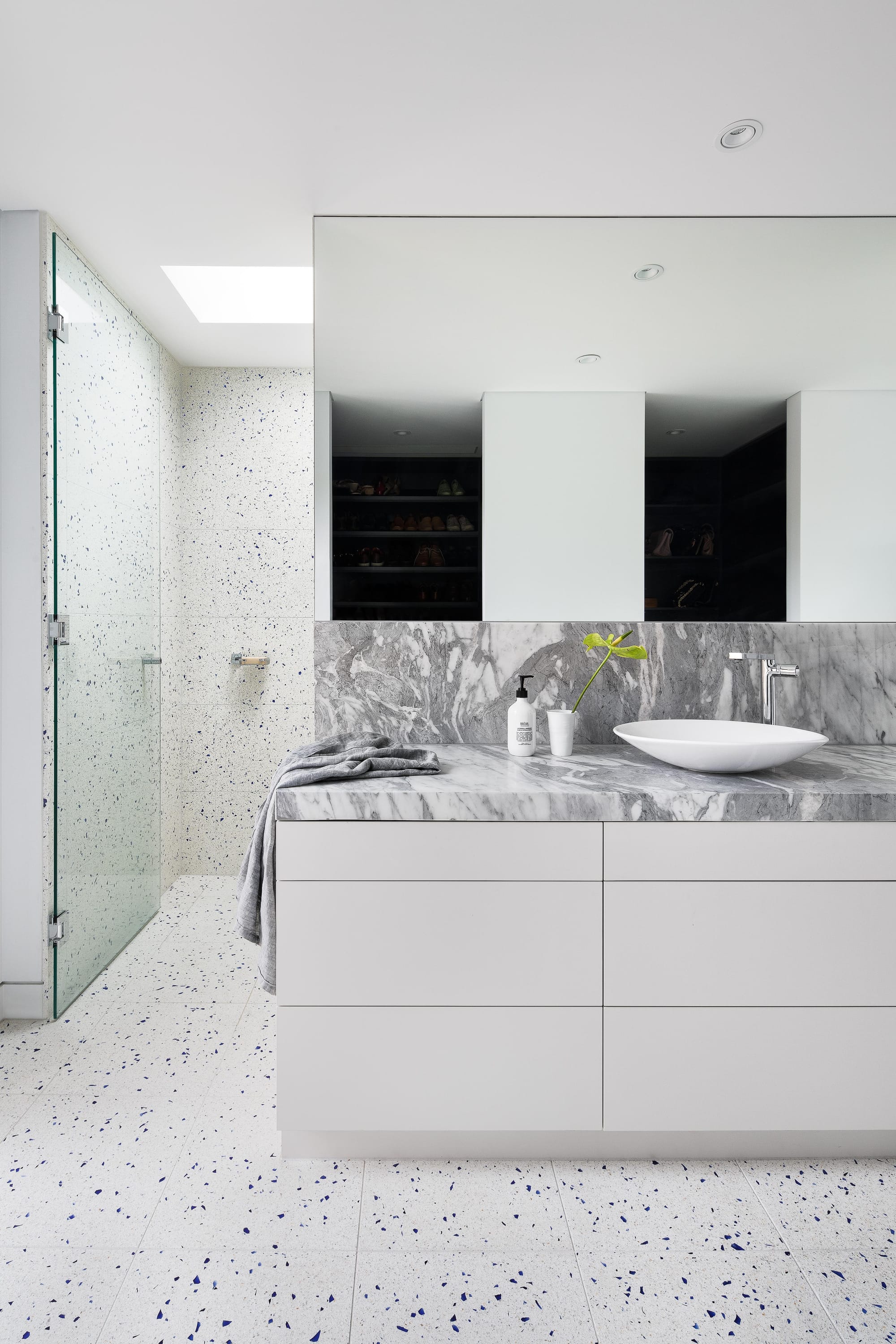 Cremorne House by Trethowan. Photography by Emily Bartlett. Residential bathroom with white cabinetry and grey marble benchtop. White and blue-specked tiles on floor and up walls.