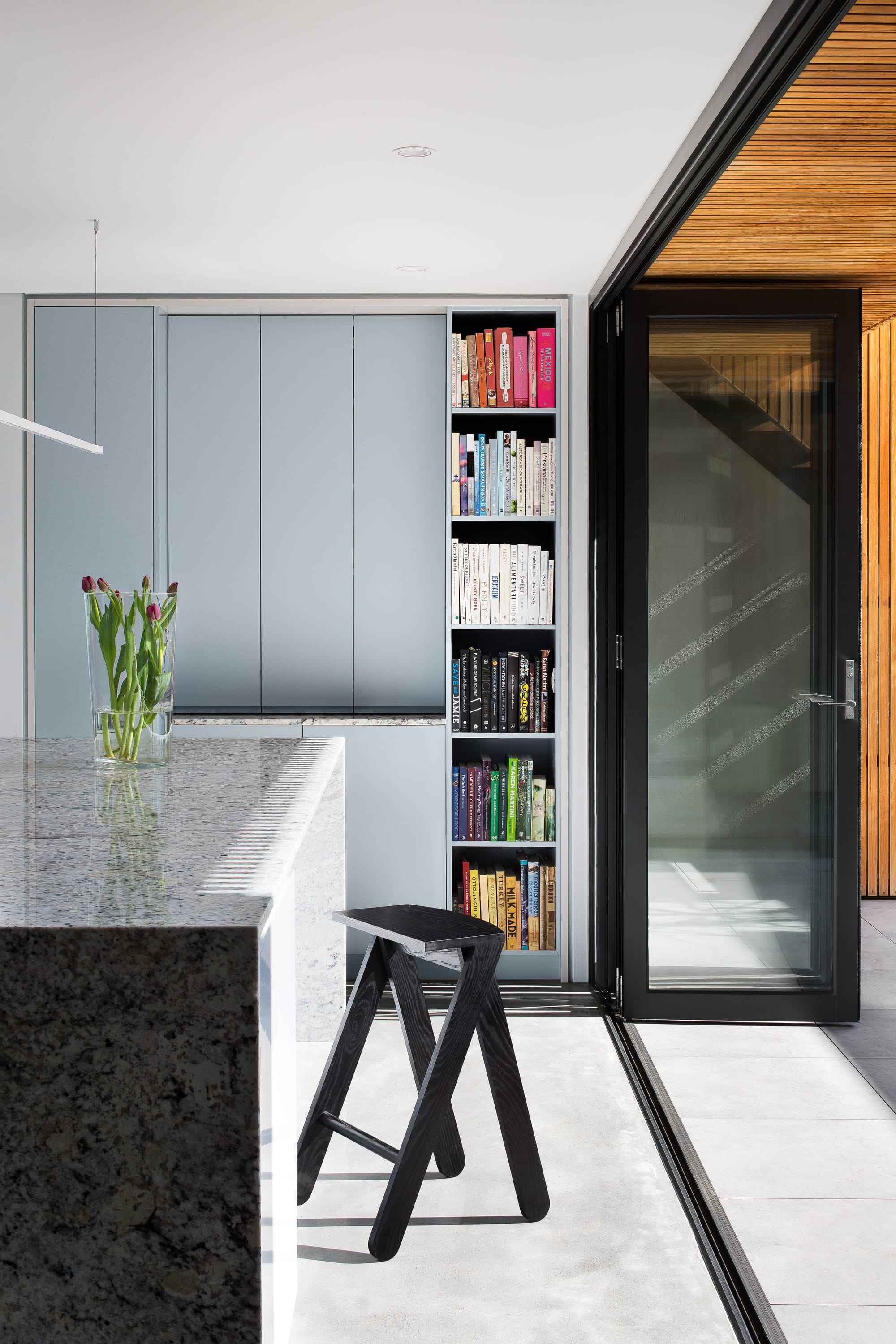 Cremorne House by Trethowan. Photography by Emily Bartlett. Residential kitchen with granite island benchtop and polished concrete floors. Bi-fold, black framed doors open onto external courtyard. 