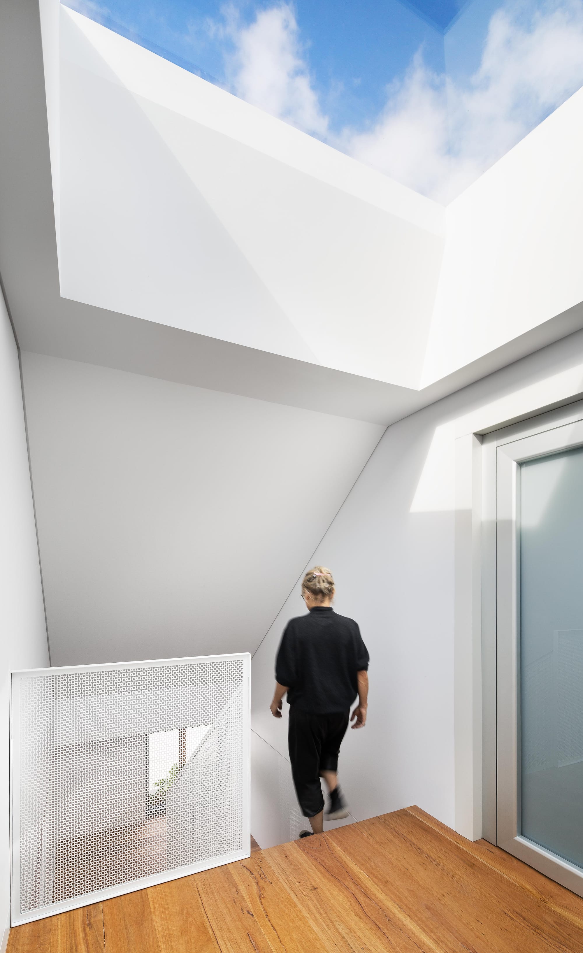 An internal shot of the staircase with a white metal balustrade and large skylight above