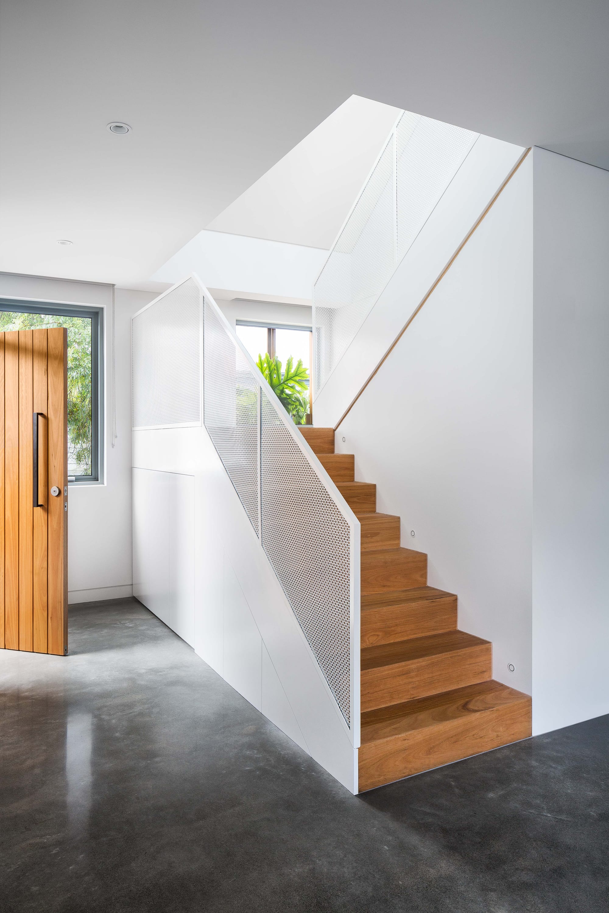 Cremorne House by Trethowan. Photography by Emily Bartlett. Timber staircase with white perforated metal balustrade. Polished concrete floor, white walls and timber door.