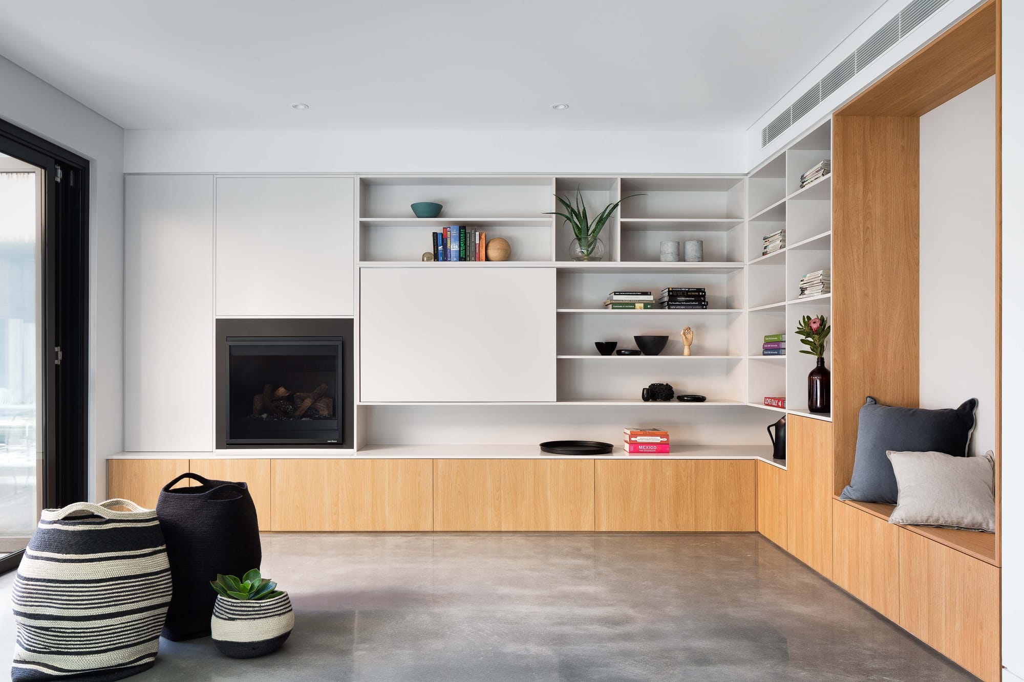 Cremorne House by Trethowan. Photography by Emily Bartlett. Residential living space with polished concrete floors and integrated timber joinery. Black fireplace to the left. 