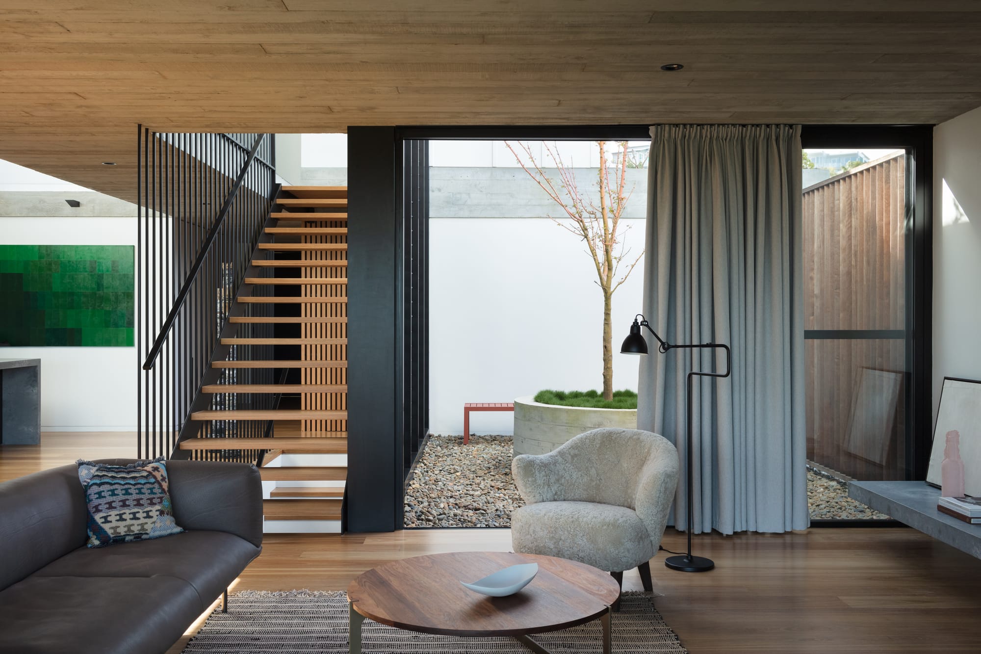 Grandview House by Ian Bennett Design Studio. Photography by Clinton Weaver. Living space with timber floors and staircase, with black balustrade. Pebble floor courtyard in background. 