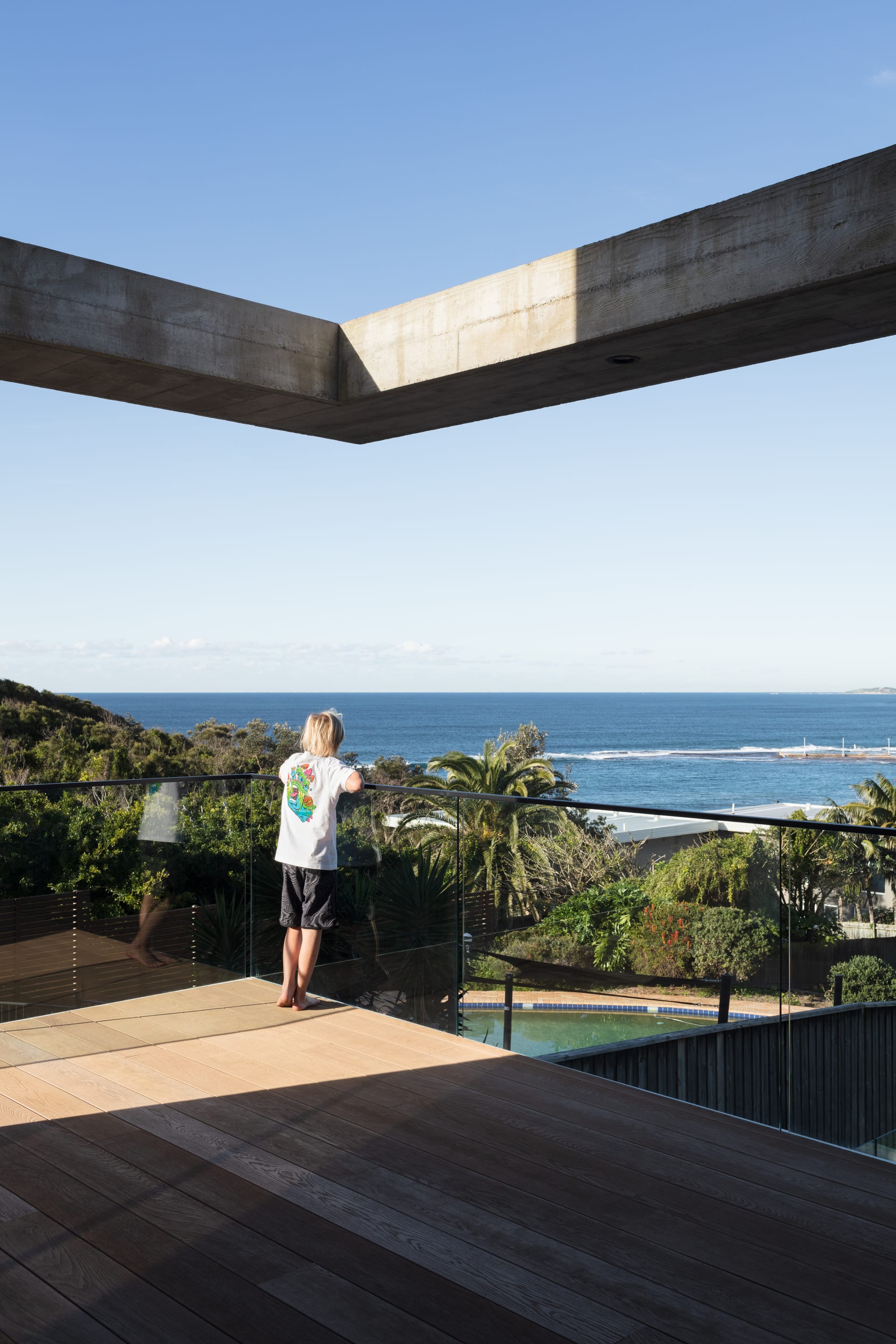 Grandview House by Ian Bennett Design Studio. Photography by Clinton Weaver. Balcony overlooking beach. Timber decking and concrete features. Glass railing. 
