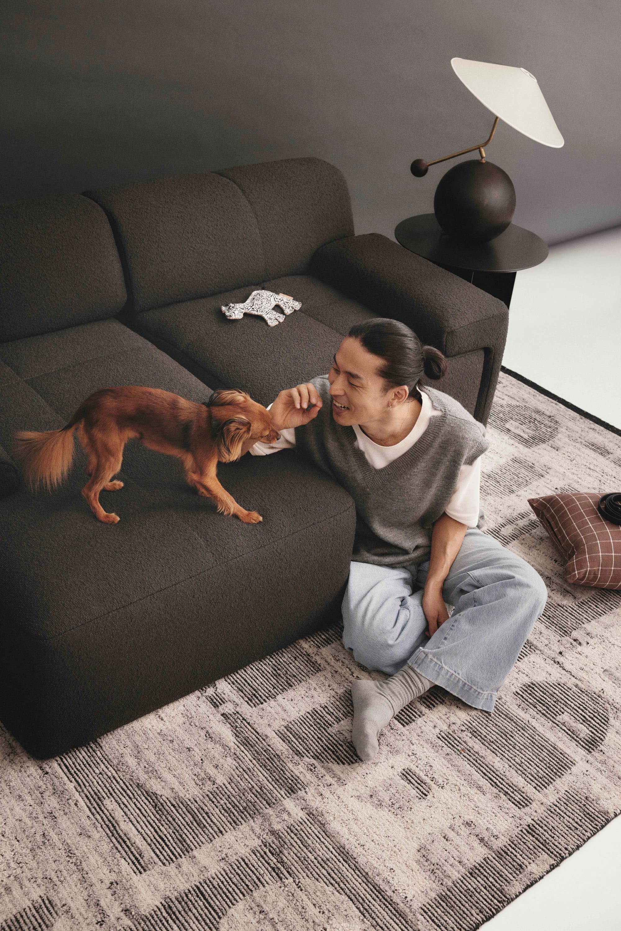 Eva Everyday Sofa. Copyright of Eva. Man plays with a dog on a graphite boucle modular sofa. 