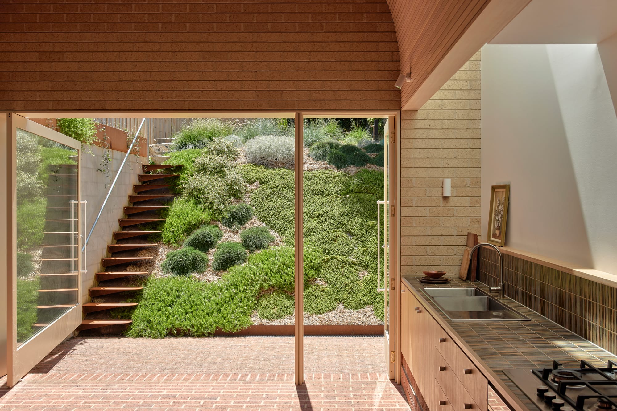 Harriet's House by SO:Architecture. Photography by Sean Fennessy. Landscape of transition from inside to out with brick flooring throughout. Sloping garden with staircase.