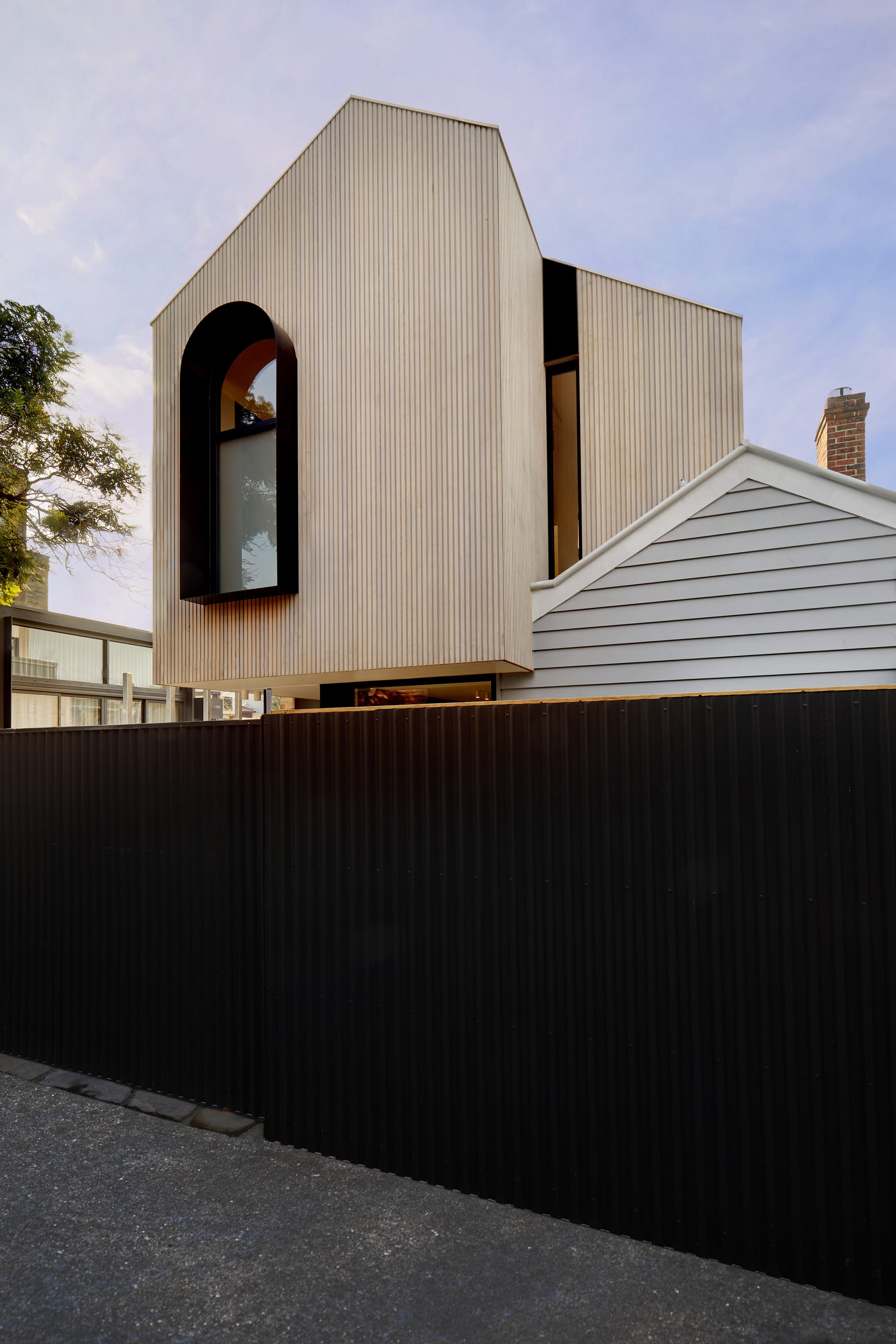 The Full Monty by FYC Architects. Photography by Stephanie Rooney. Exterior facade of home with timber clad second storey with gabled roof and bold, black window frame. Black fence encloses ground floor from footpath. 