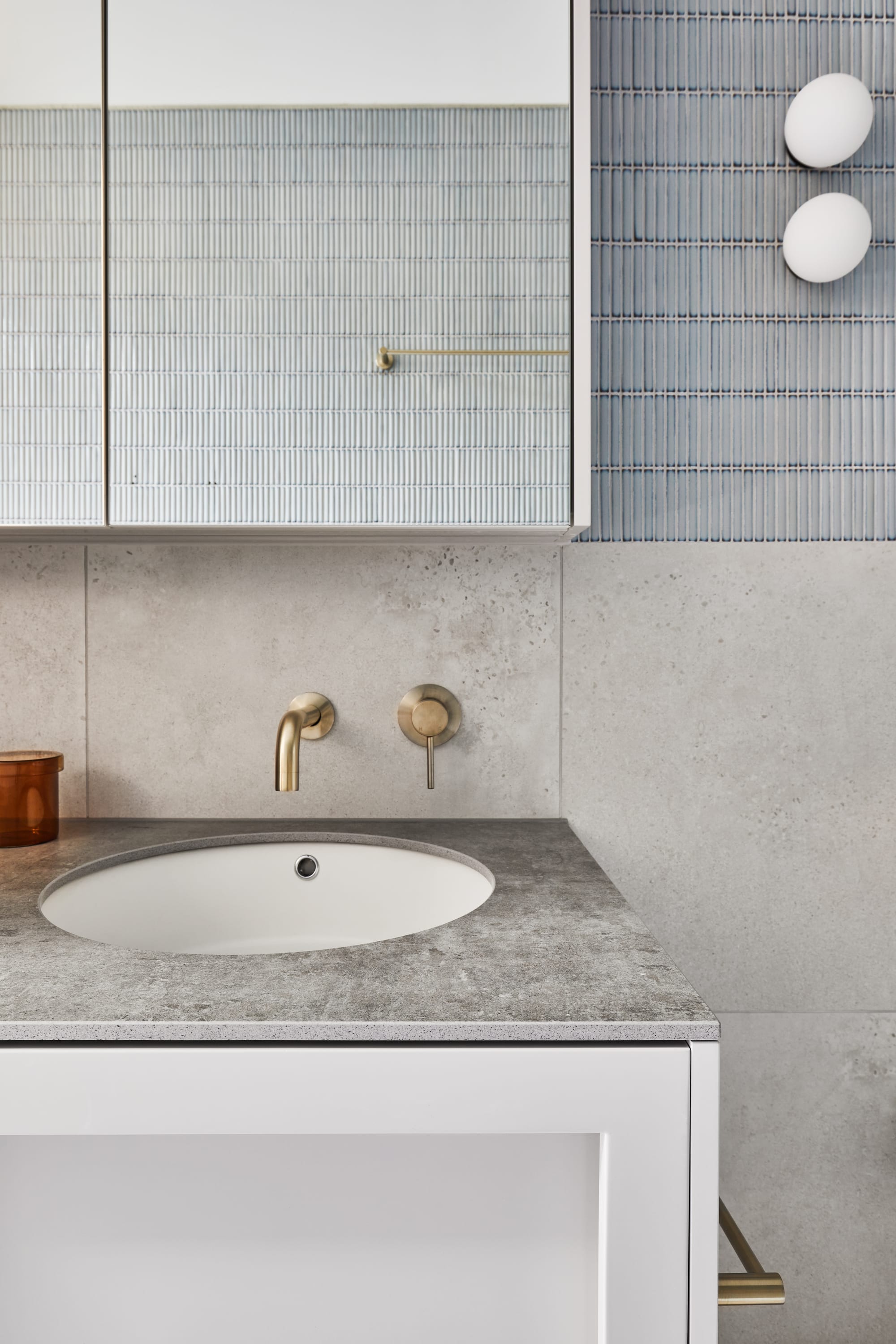 The Full Monty by FYC Architects. Photography by Stephanie Rooney. Muted bathroom counter with grey stone benchtop and brass tapware. Feature blue finger tiles on wall. Large square mirror. 