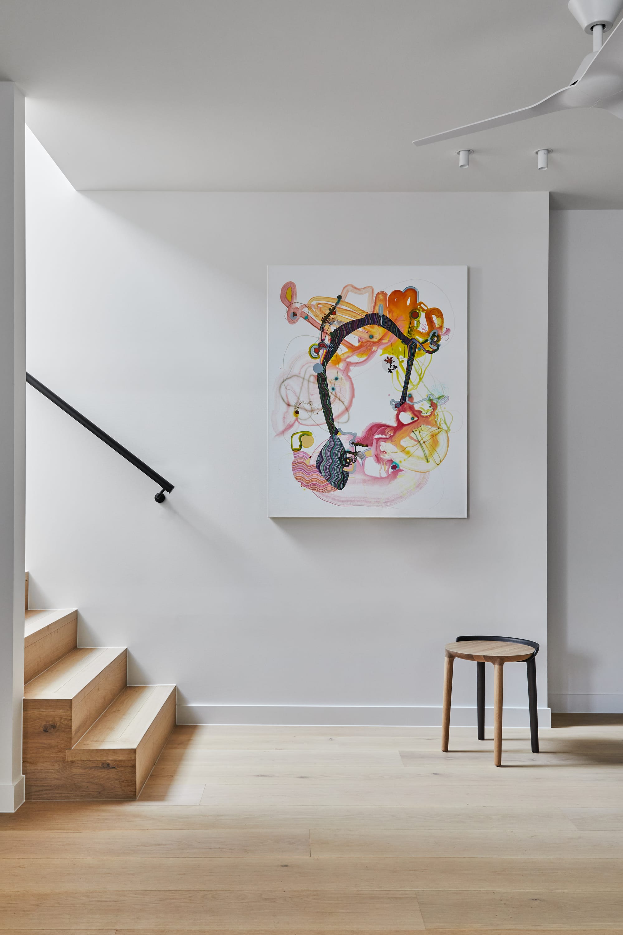 The Full Monty by FYC Architects. Photography by Stephanie Rooney. Timber stairs seen elevating behind white walls. Abstract art hangs on wall in front of stairs. 