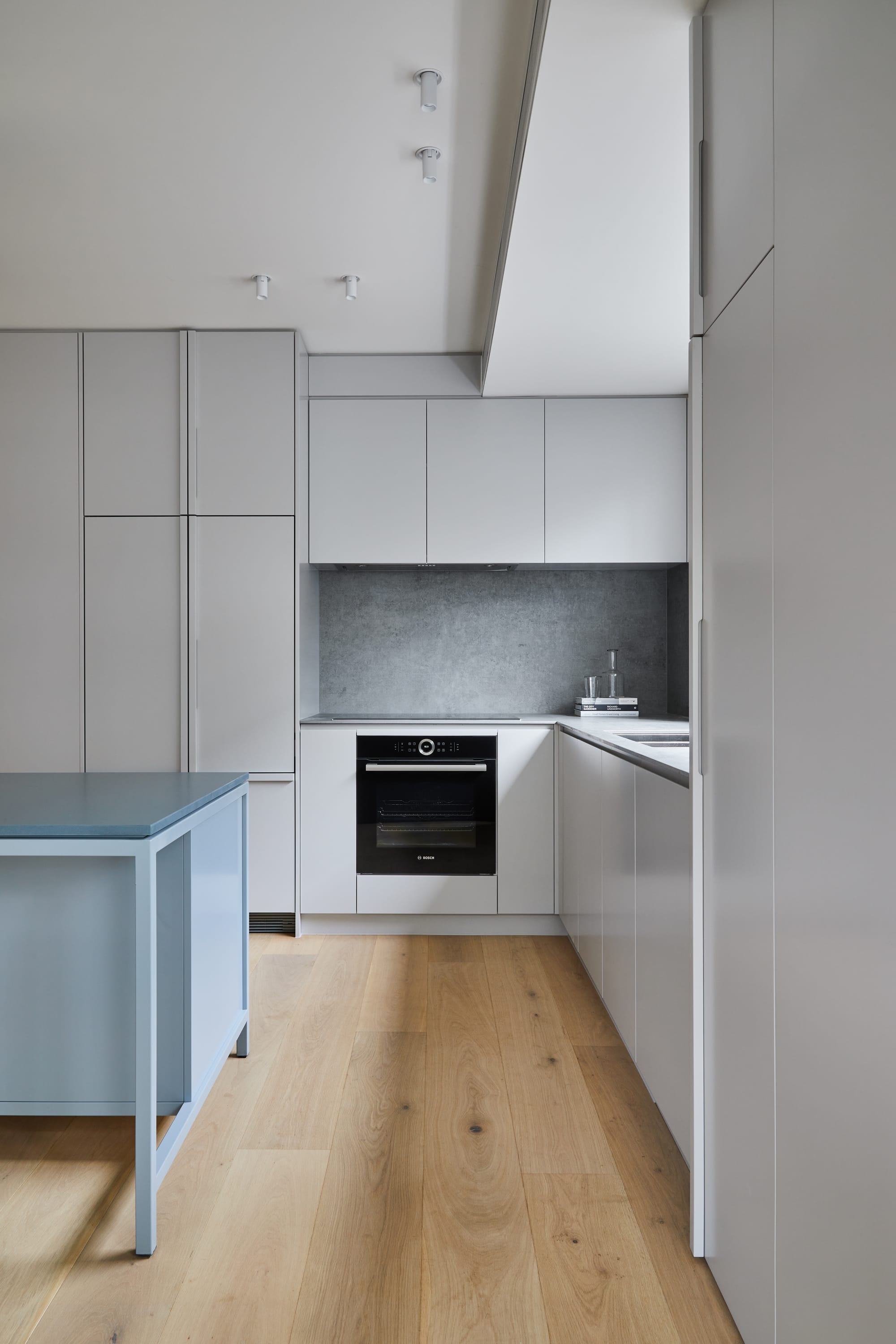 The Full Monty by FYC Architects. Photography by Stephanie Rooney. Residential kitchen with grey cabinetry, pale timber floors and blue island bench. Concrete-look splashback. 