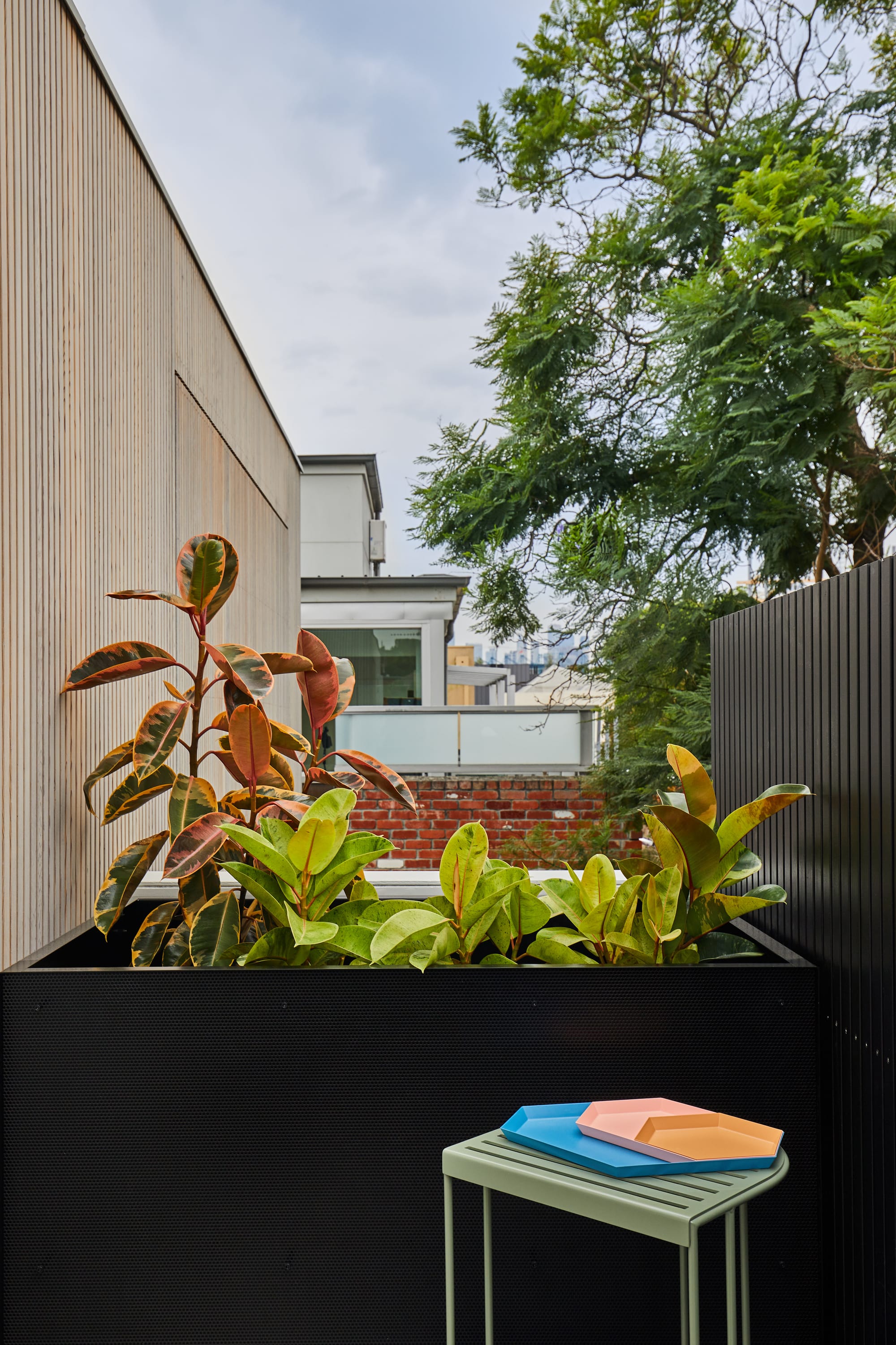 The Full Monty by FYC Architects. Photography by Stephanie Rooney. City skyline views visible from upper storey balcony. Large black planter separates balcony from neighbours. 