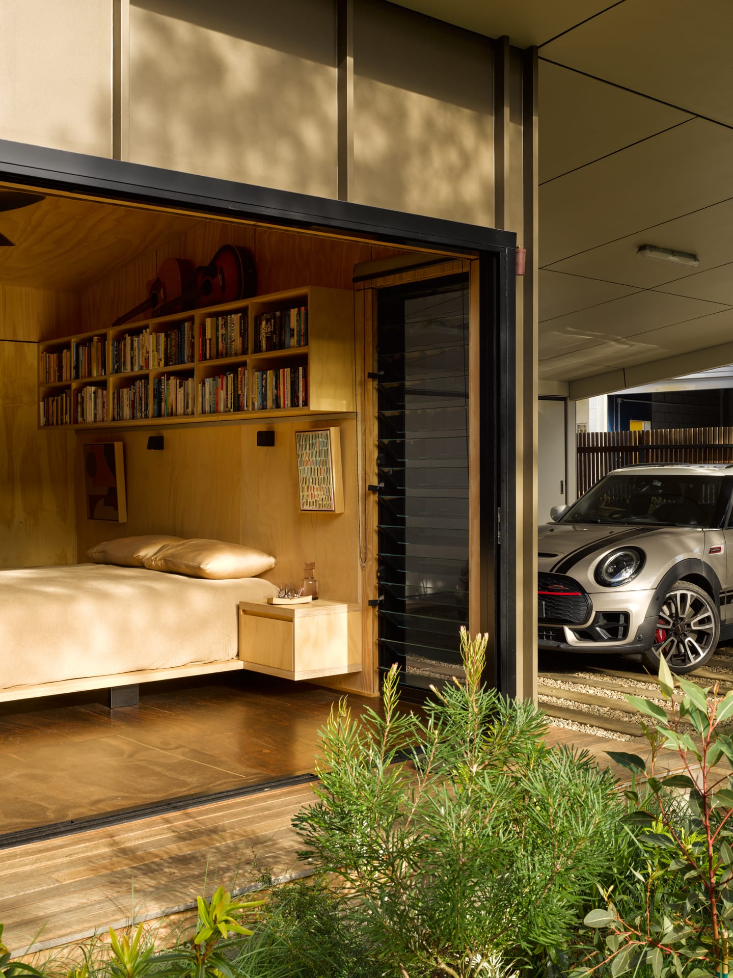 PaperBark Pod by Bark Design. Photography by Christopher Frederick Jones. Interior bedroom opened up onto gardens. Carport with small car to right of image. Bedroom panelled in plywood. 